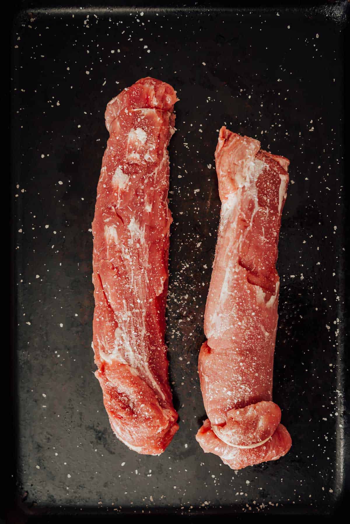 Two pork tenderloins on a black tray.