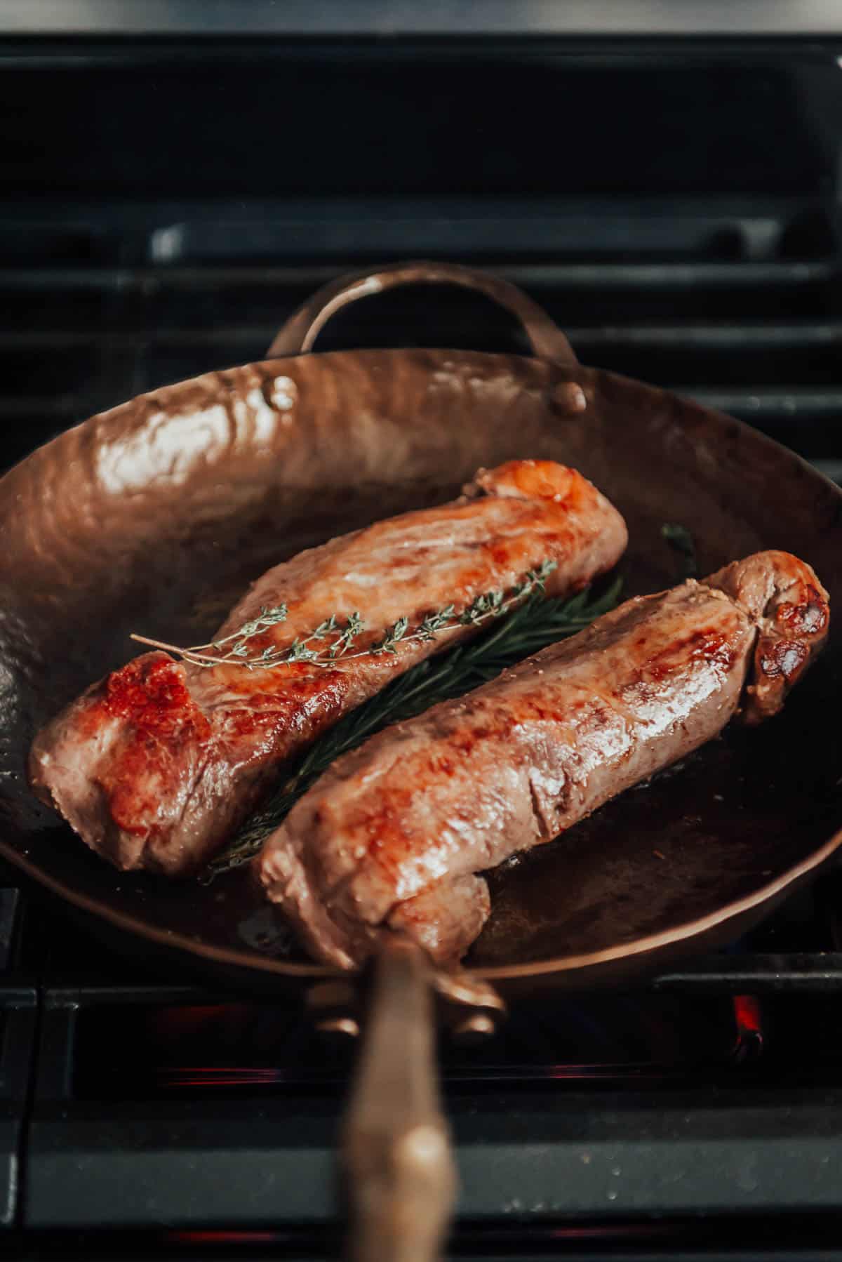 Two pork tenderloins in a frying pan on a stove.