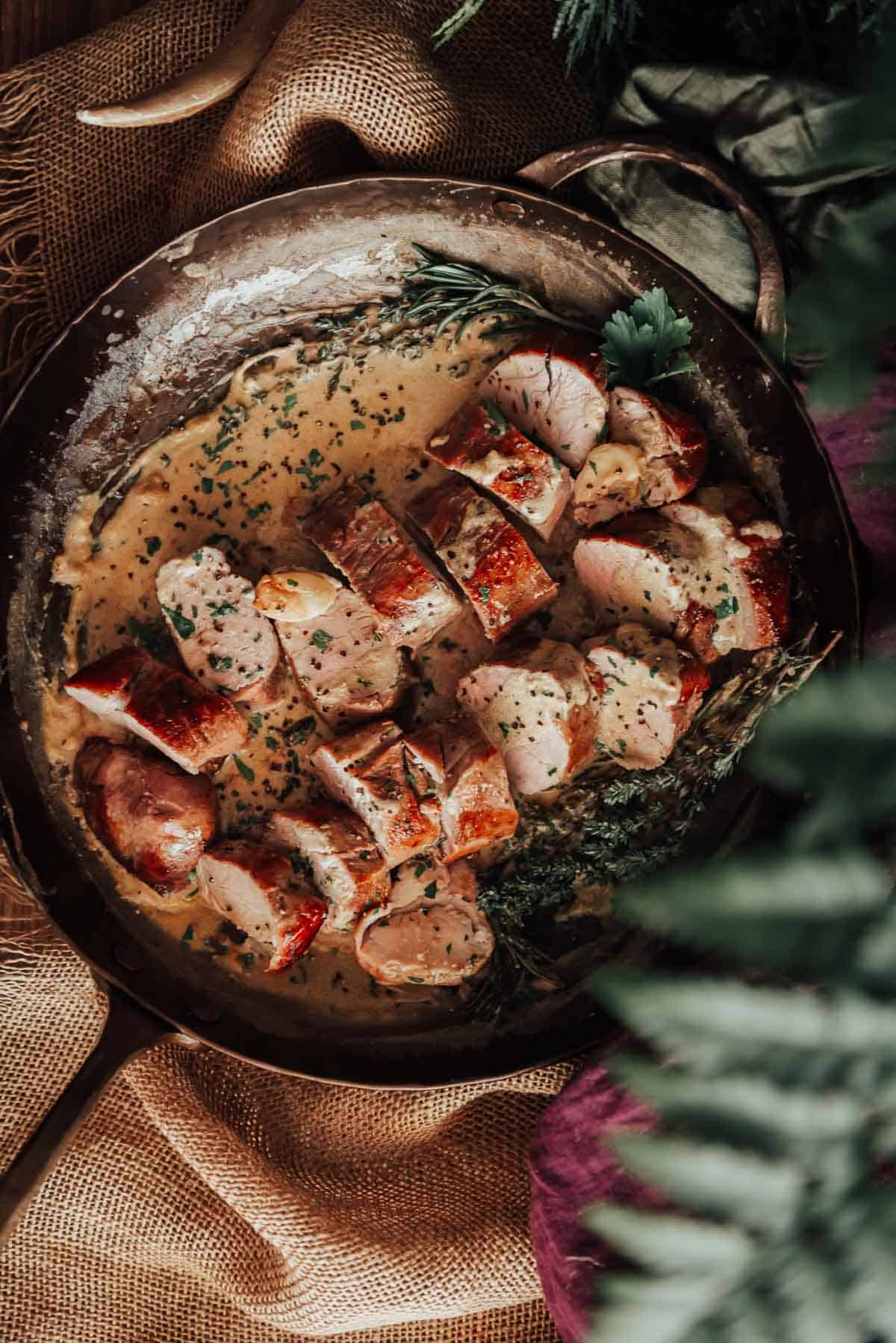 A frying pan with pork tenderloin and herbs on it.