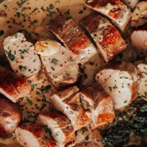 Pork tenderloin in a pan with sauce and herbs.