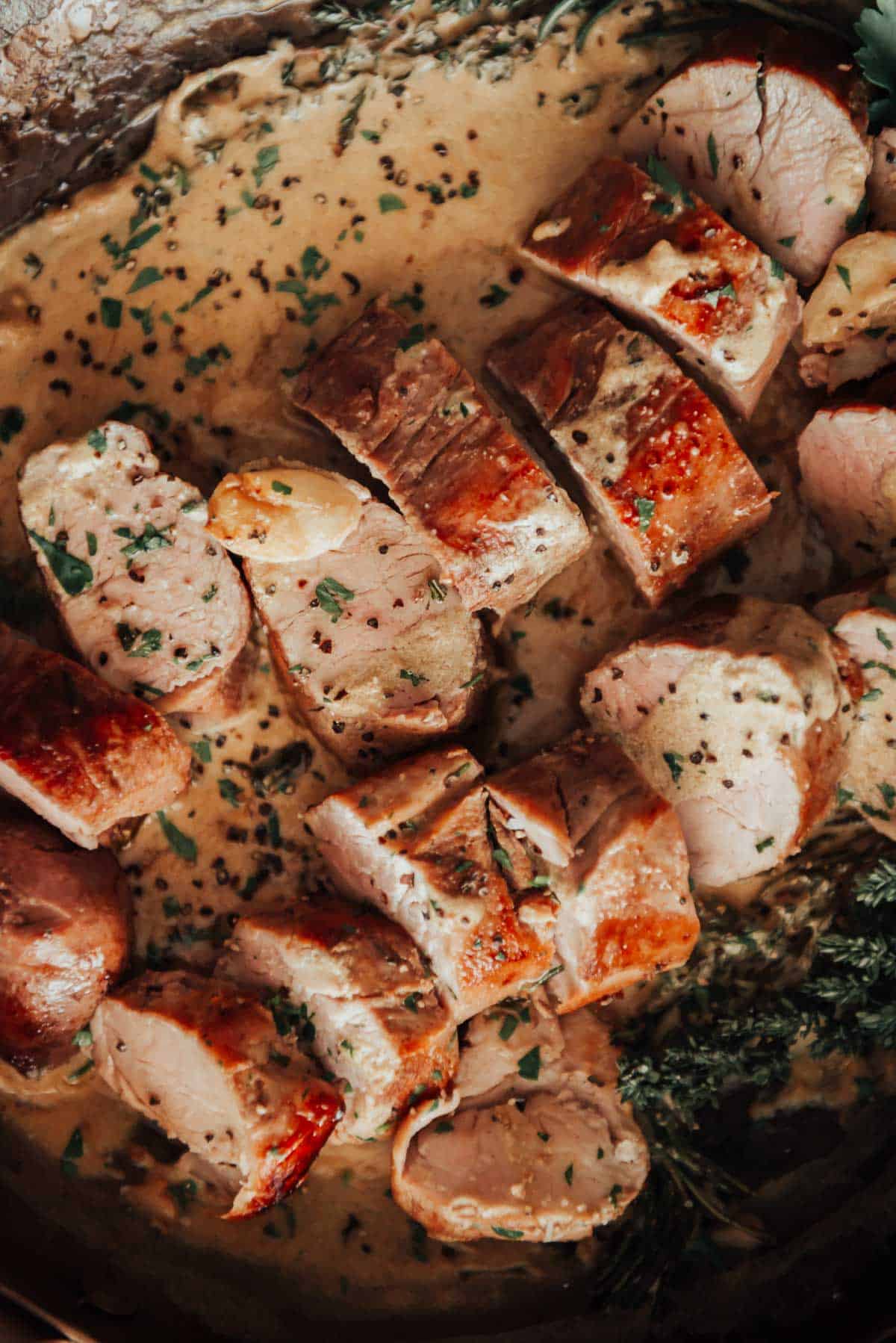 Pork tenderloin in a pan with sauce and herbs.