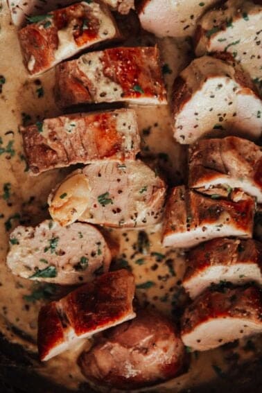 Pork tenderloin in a pan with sauce and herbs.