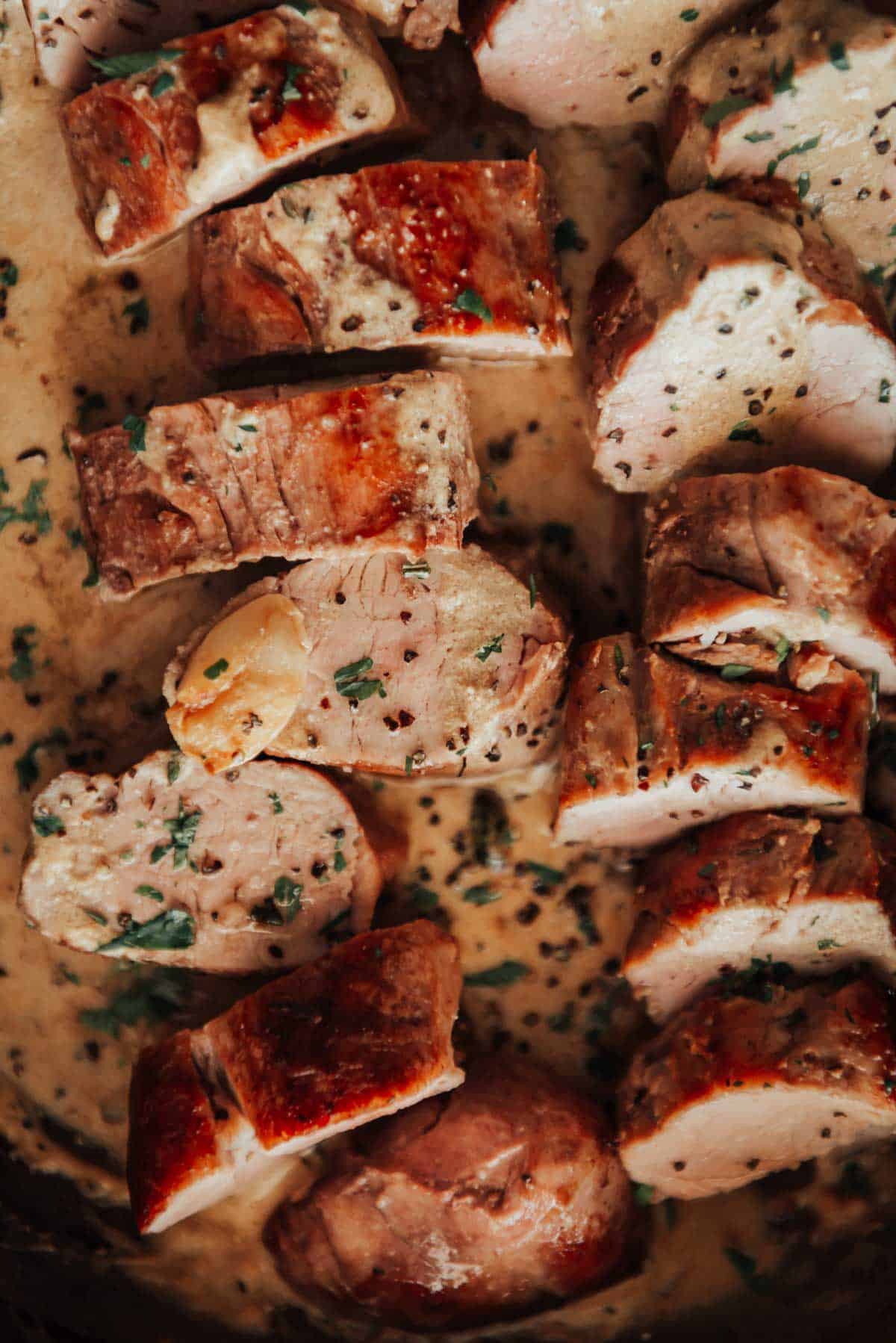 Pork tenderloin in a pan with sauce and herbs.