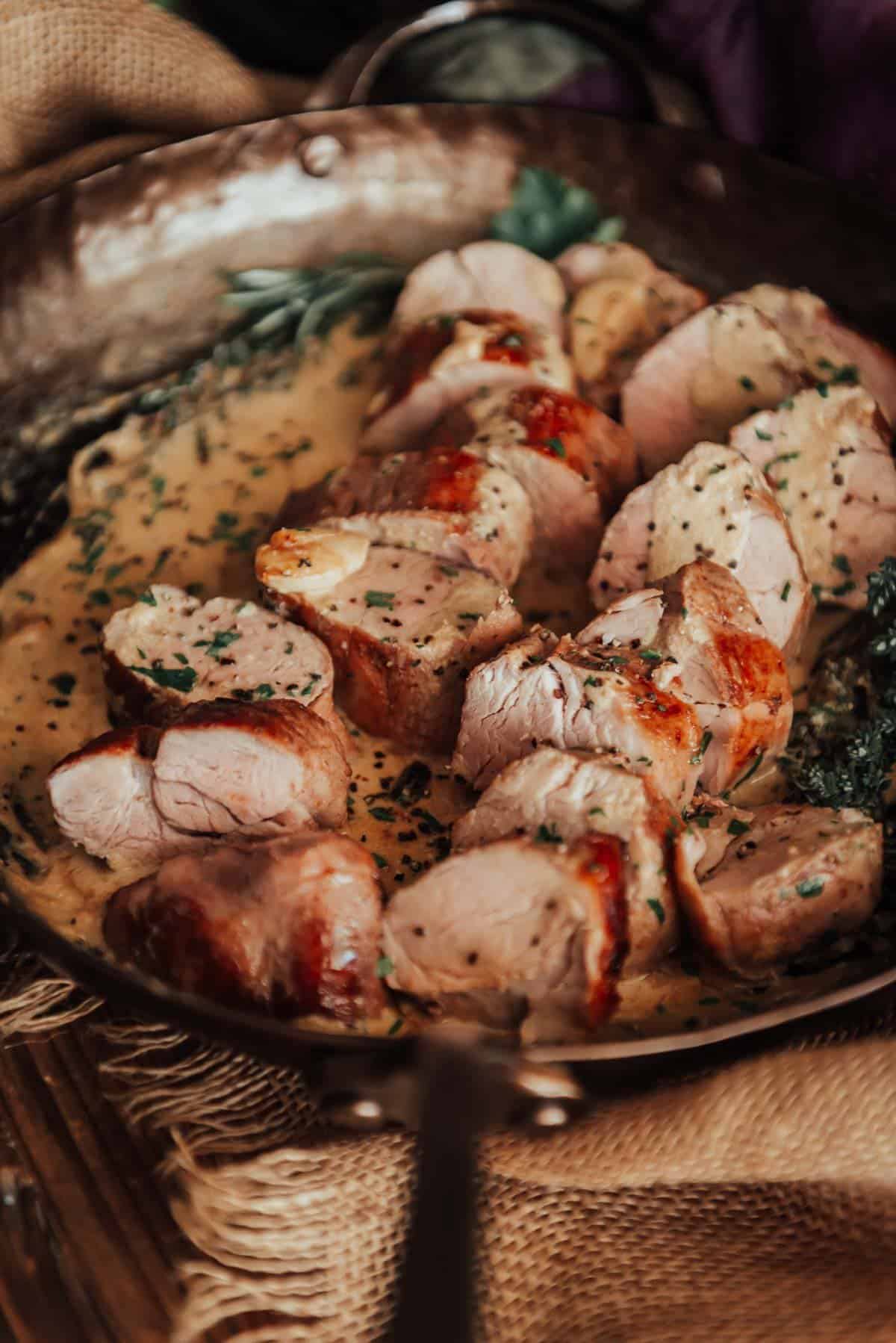 Pork tenderloin in a pan with mustard cream sauce and herbs.