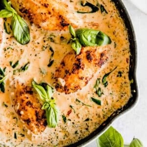 Sautéed chicken breasts in a creamy sauce garnished with basil leaves, served in a skillet.