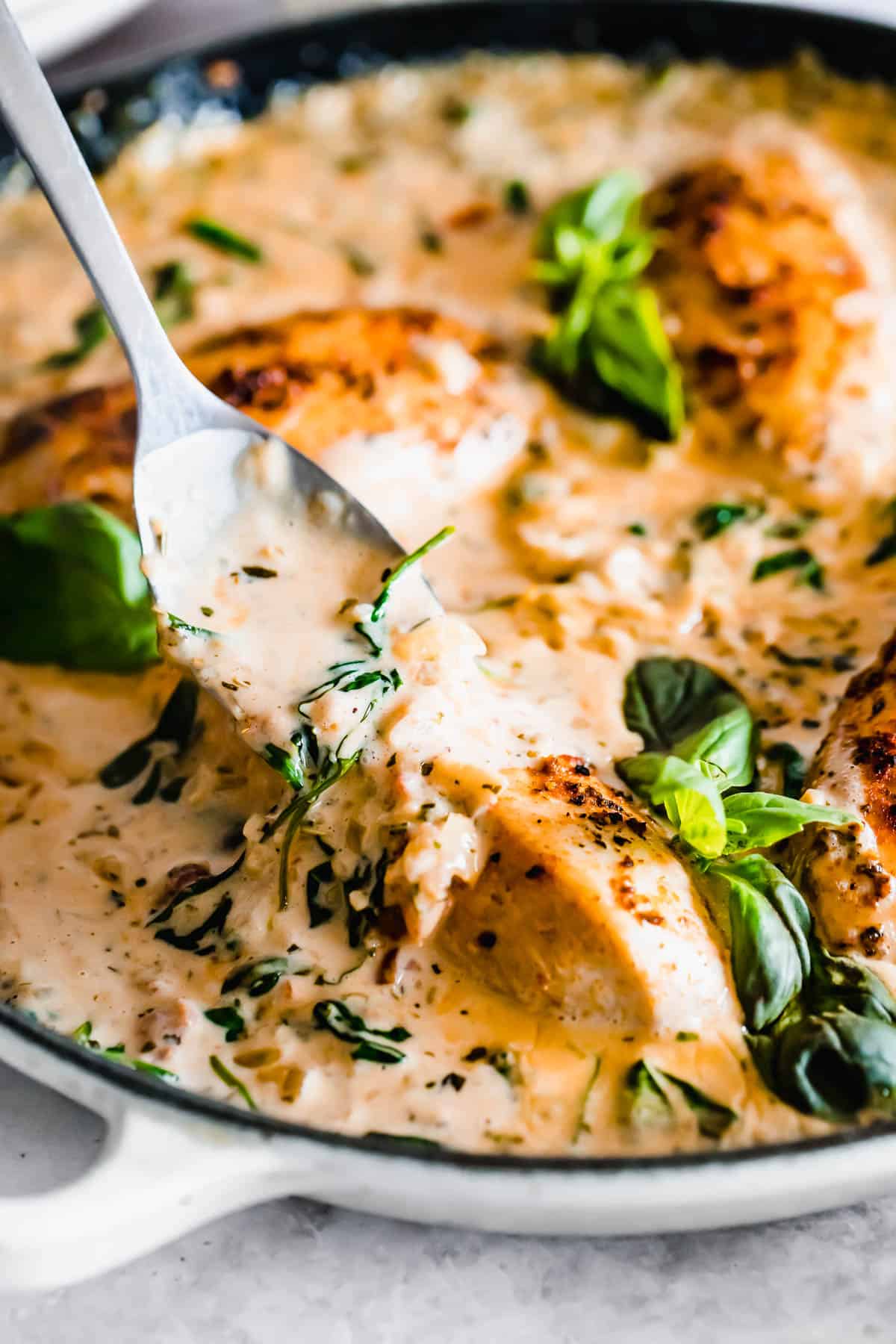 Sautéed chicken breasts in a creamy sauce garnished with basil in a skillet, with a serving spoon.