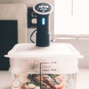 A sous vide cooker attached to a clear container filled with water and various foods, displaying a temperature of 124.5 degrees Fahrenheit.
