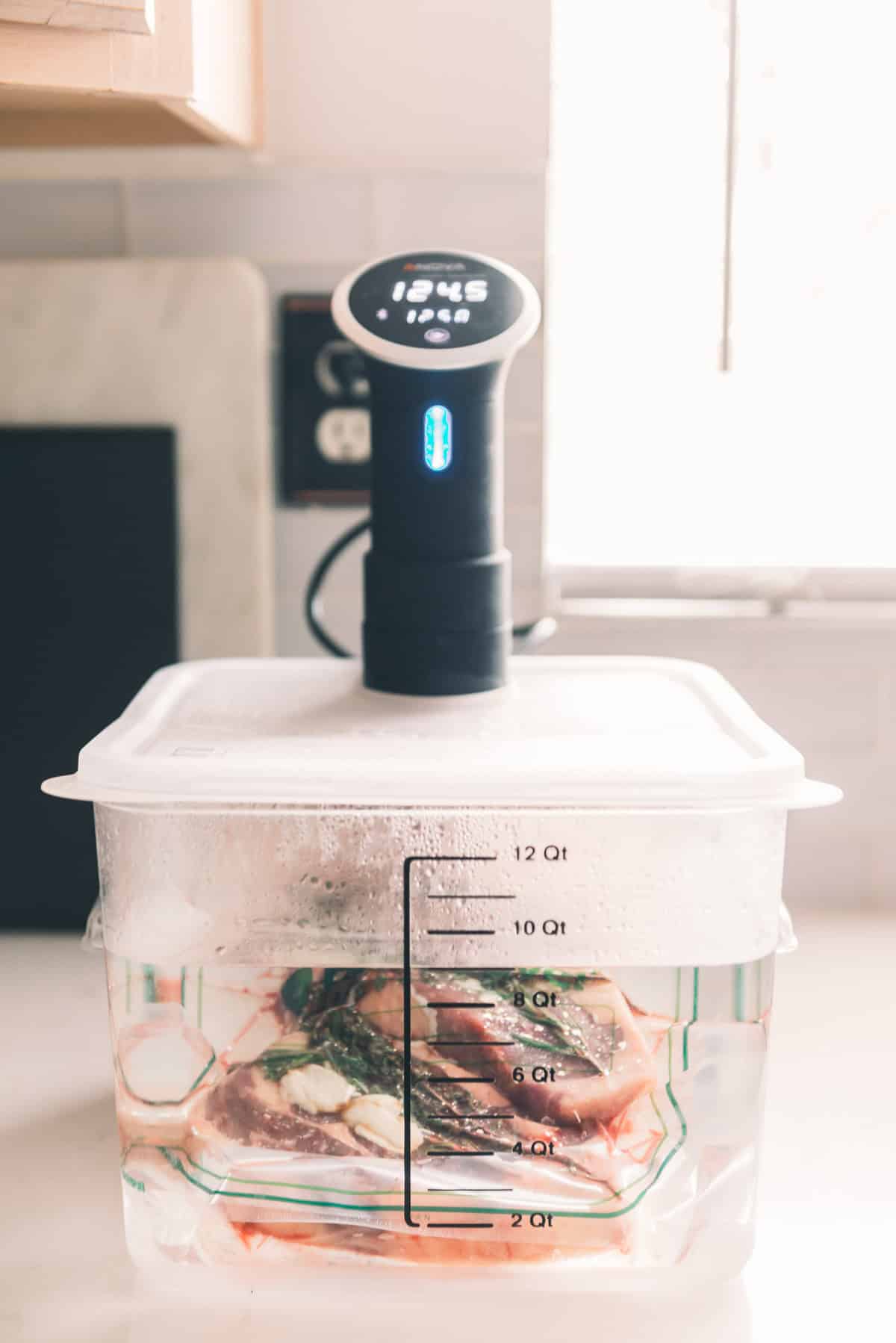 A sous vide cooker attached to a clear container filled with water and various foods, displaying a temperature of 124.5 degrees Fahrenheit.