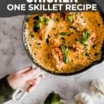 A pinterest image for a creamy tuscan chicken recipe, featuring a skillet of the dish with a hand holding it, surrounded by ingredients like garlic and basil.