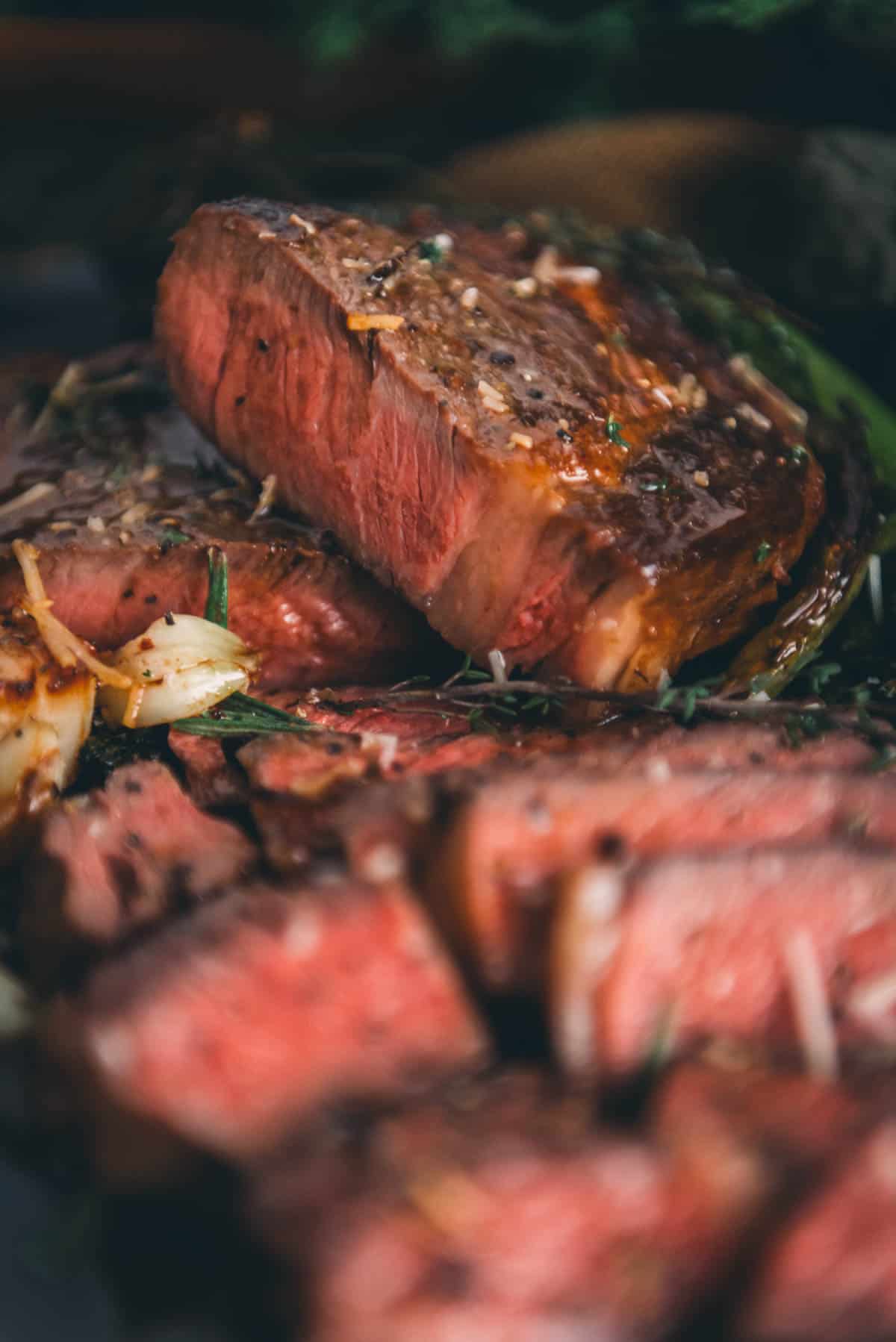 Sliced medium-rare steak seasoned with herbs and spices, focused in the foreground with a blurred background.
