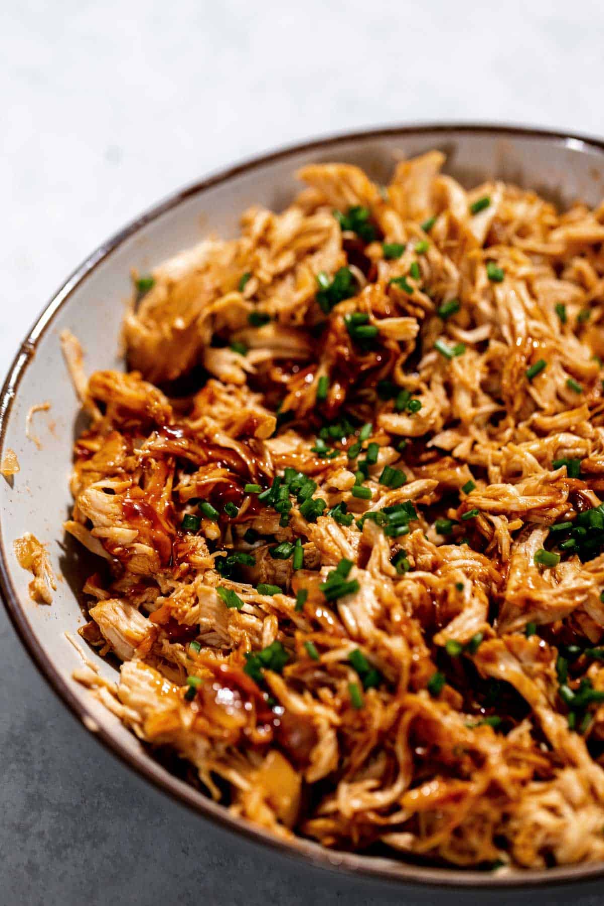 A bowl of shredded chicken topped with finely chopped green herbs and drizzled with a dark sauce.