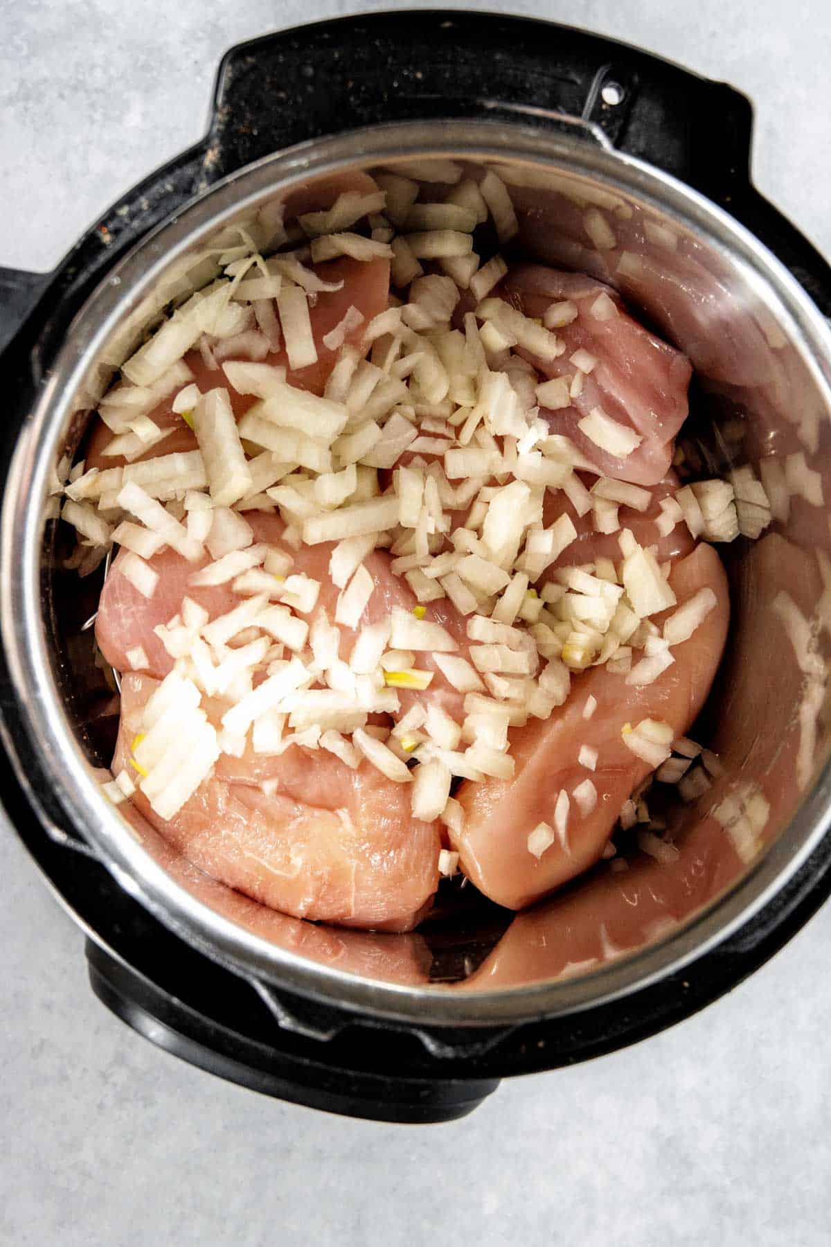 Raw chicken breasts topped with chopped onions in an Instant Pot.