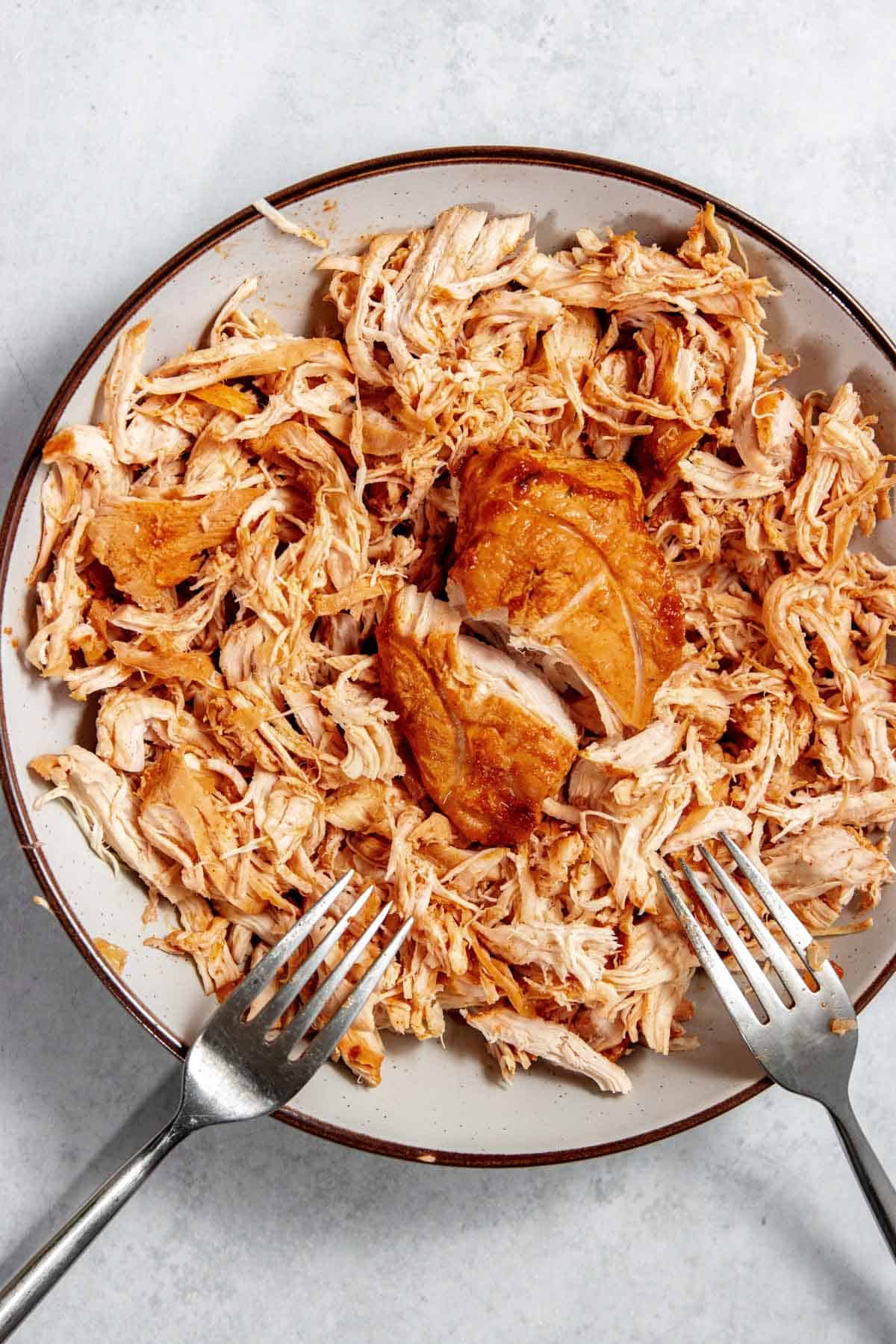 A plate of shredded chicken with two forks on the side.