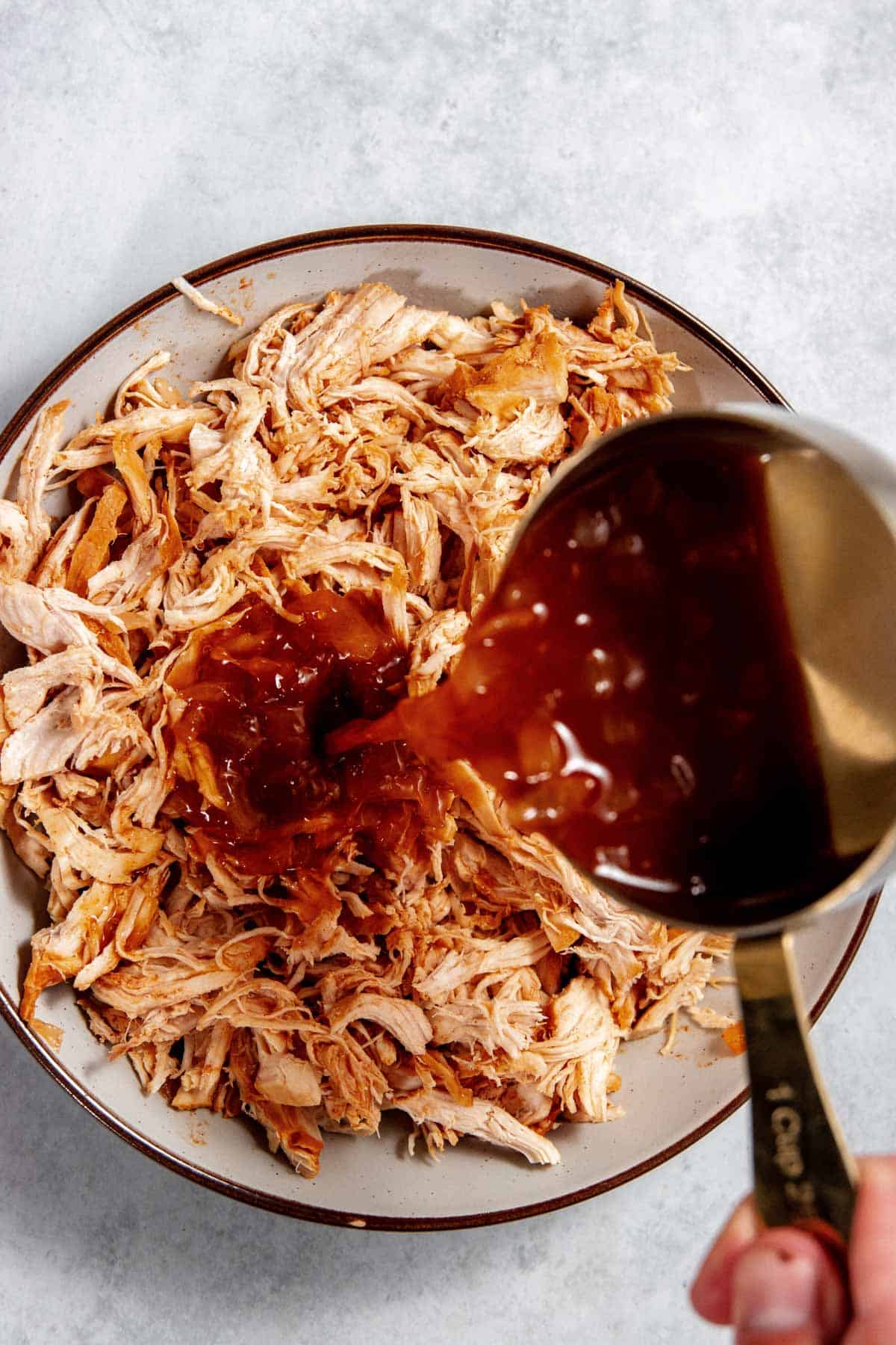 Sauce being poured onto a plate of shredded chicken.