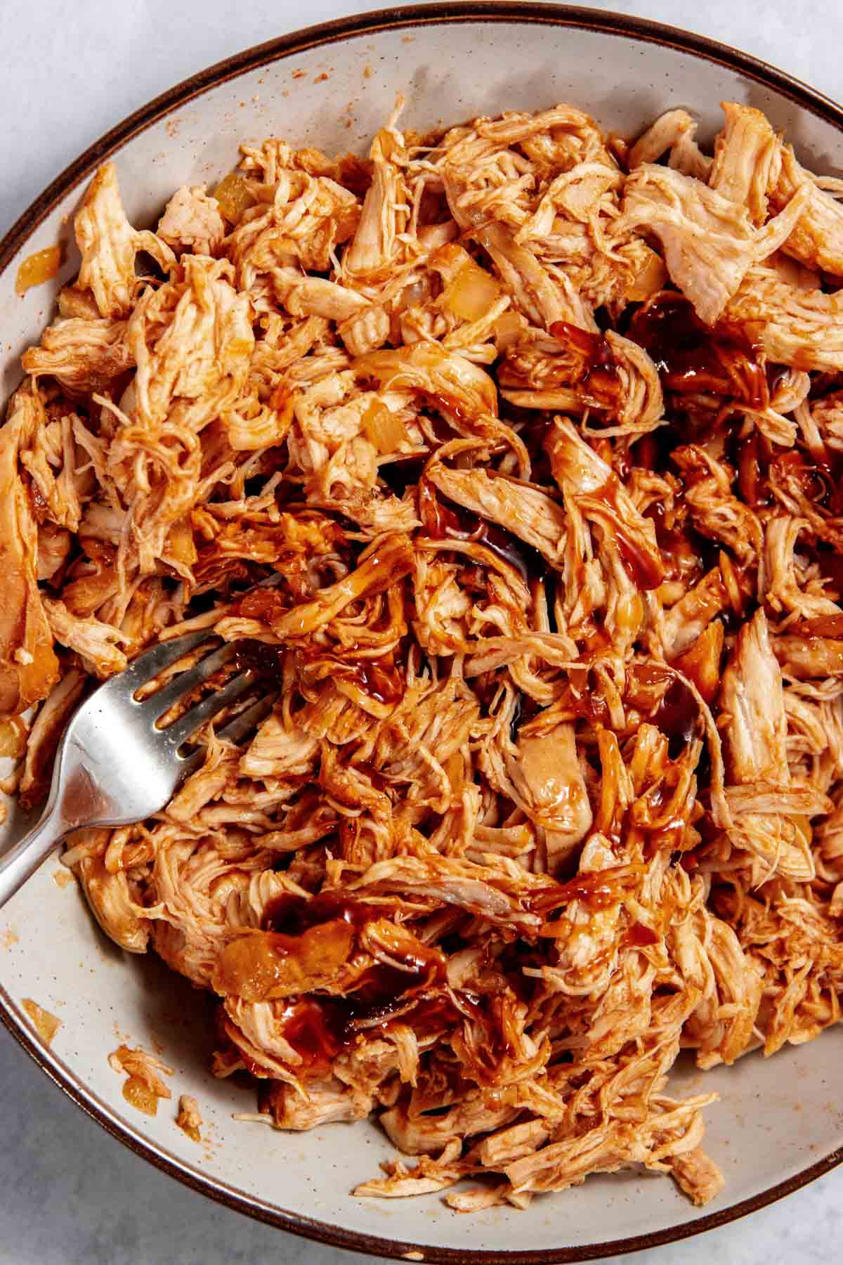 A bowl filled with shredded chicken mixed with barbecue sauce, with a fork resting on the side.