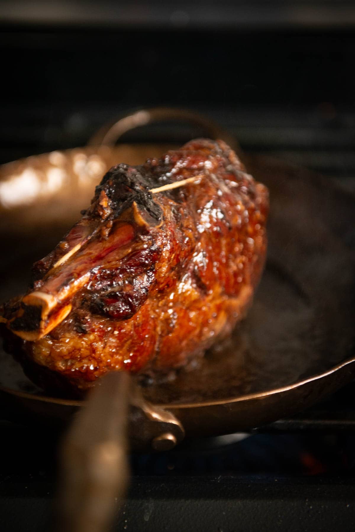 A well-cooked, browned piece of meat with a bone in a skillet on a stove.