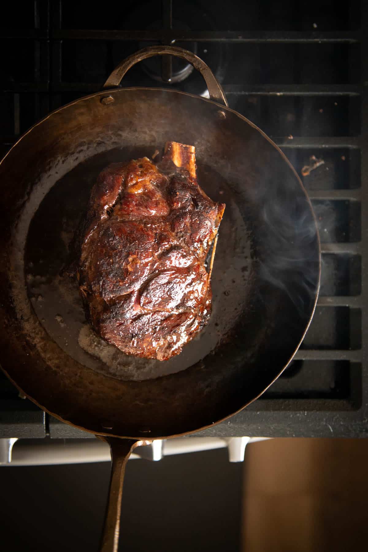 A seared steak cooking in a carbon steel skillet on a stovetop.