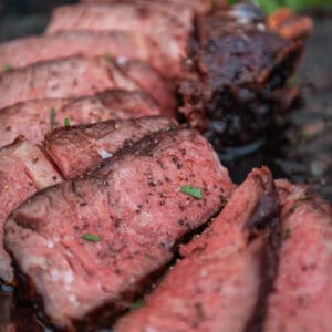 Close-up of slices of medium-rare cowboy steak on a cutting board, garnished with herbs.