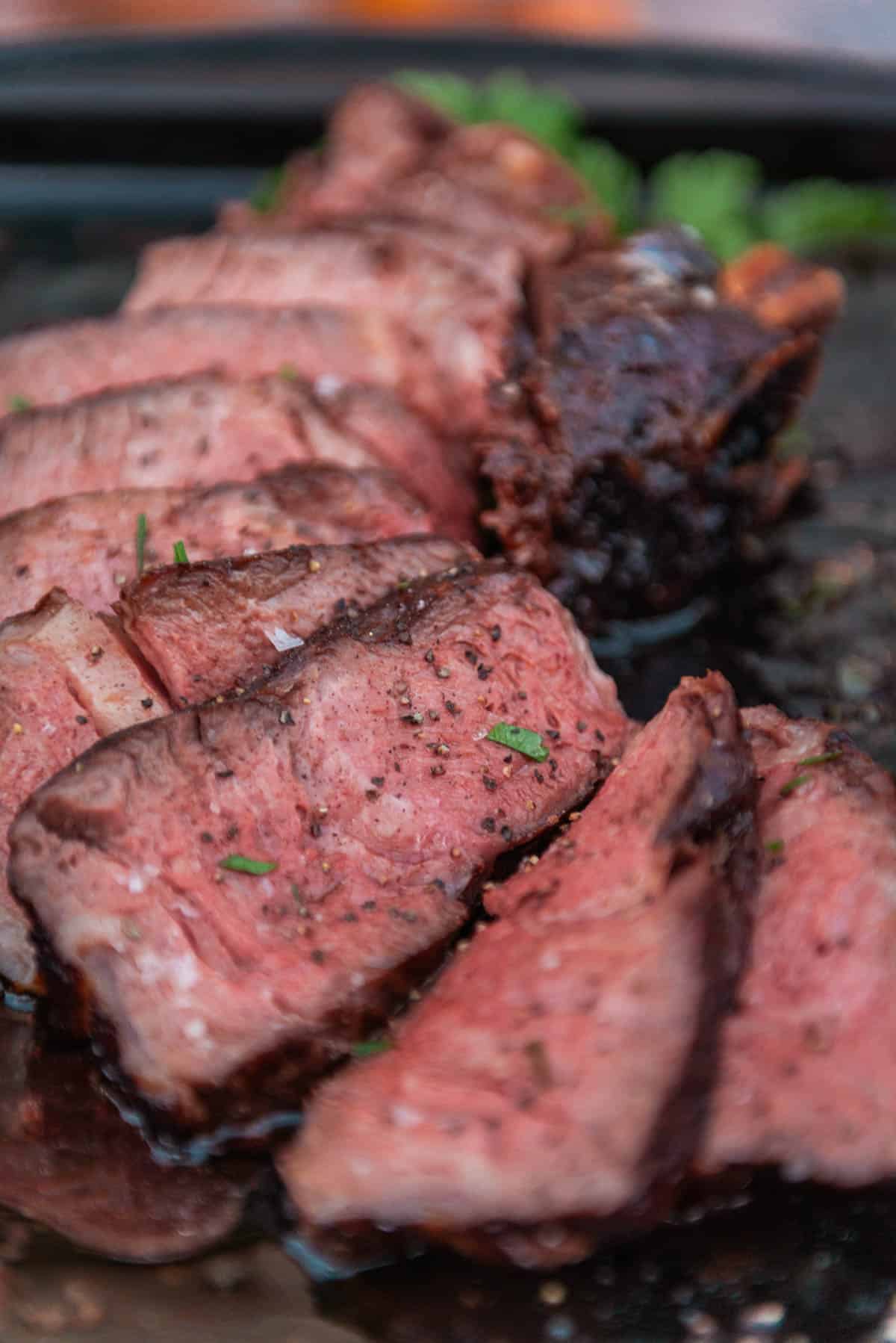 Close-up of slices of medium-rare cowboy steak on a cutting board, garnished with herbs.