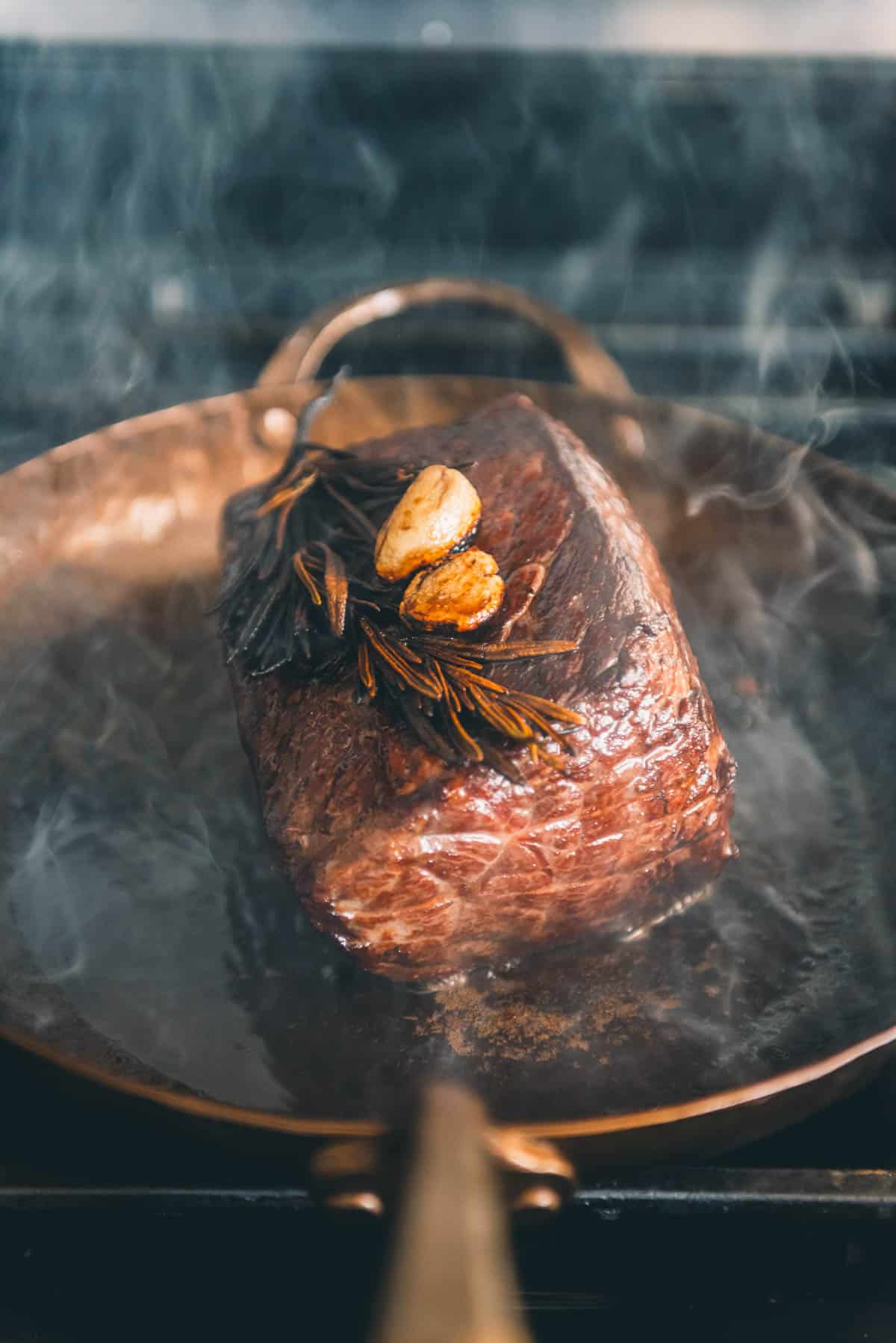 A sous vide roast beef with garlic and herbs sizzles in a copper carbon steel skillet.