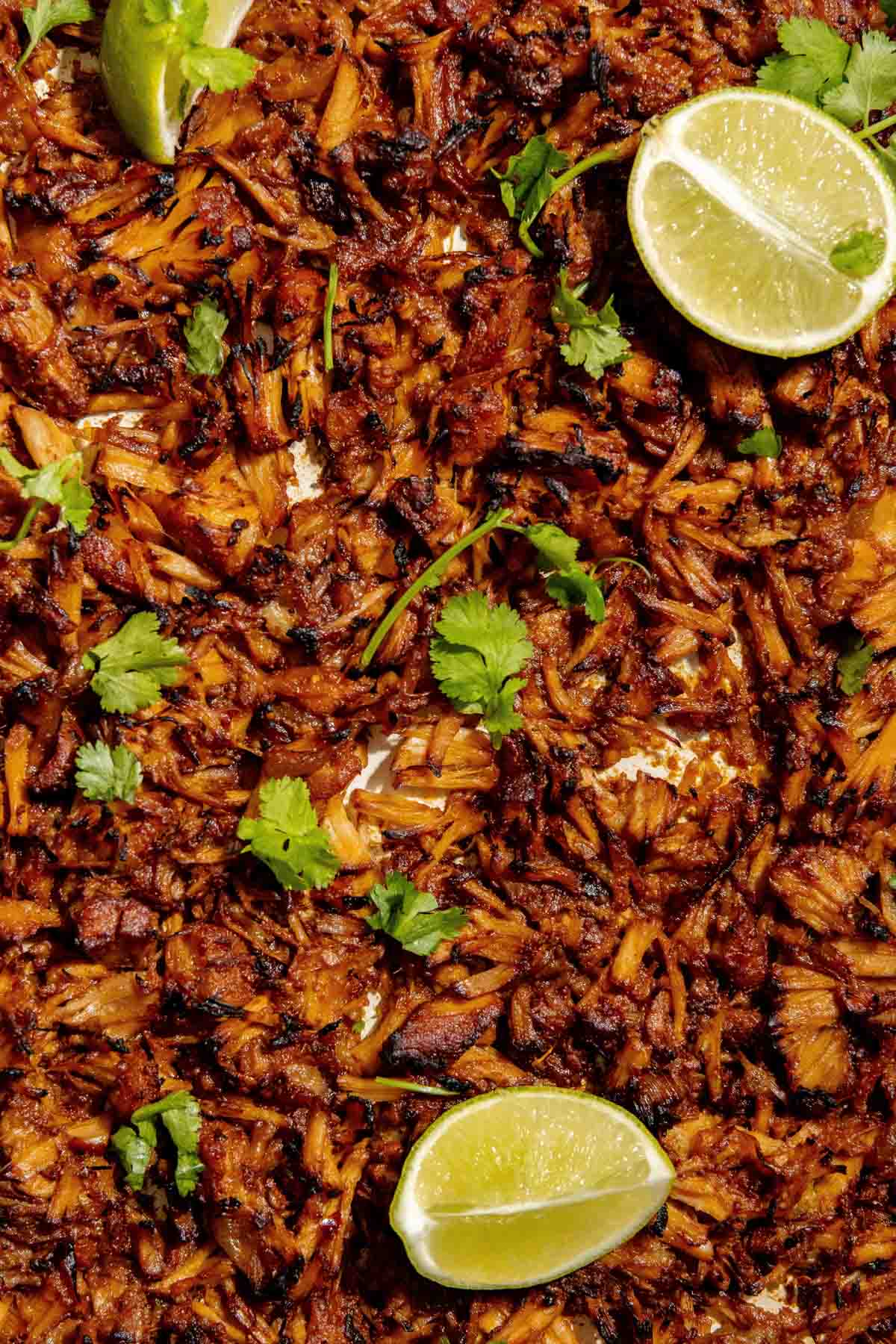 Close-up of a dish featuring seasoned and shredded carnitas, garnished with cilantro and lime wedges.