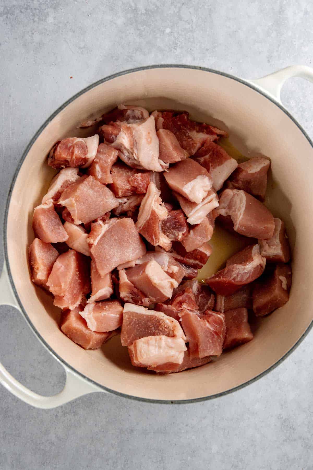 Chunks of raw pork placed in a white pot, ready for cooking.