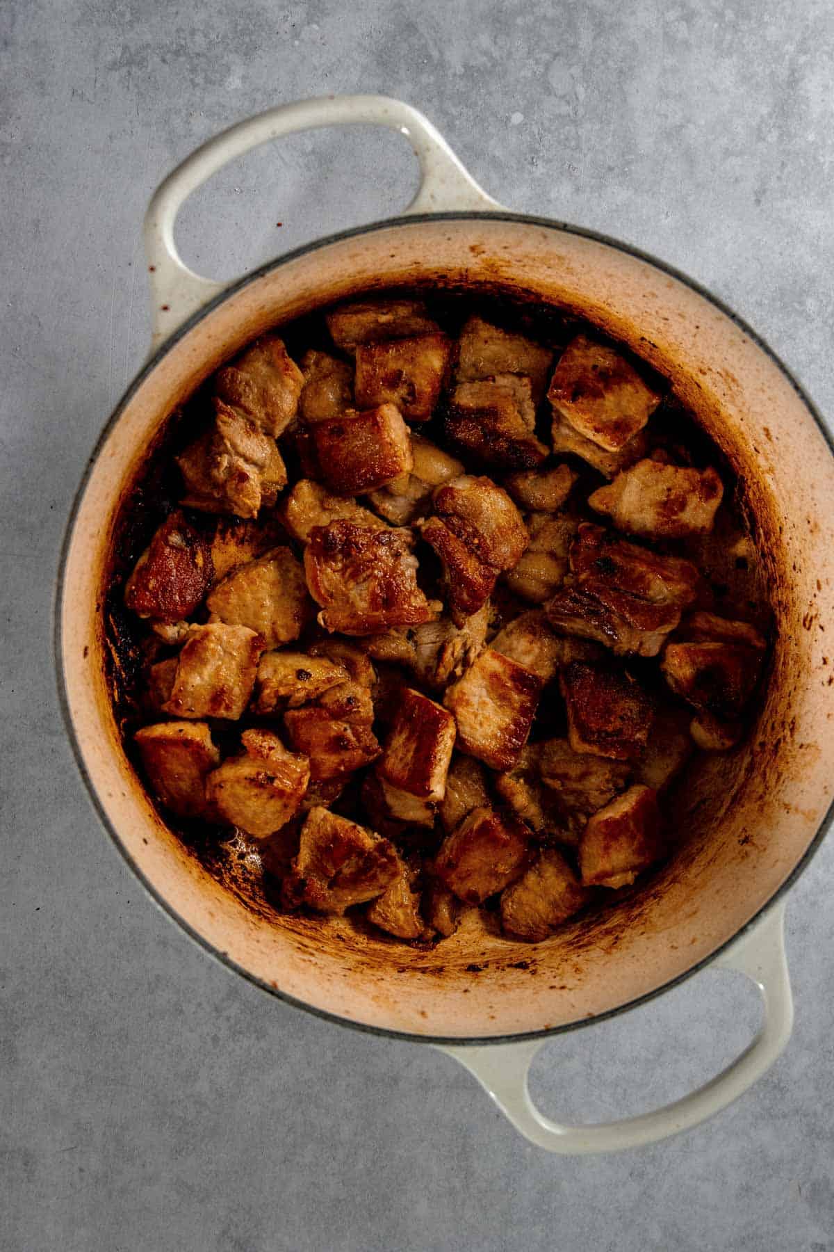 A pot filled with cooked, browned chunks of pork on a gray surface.