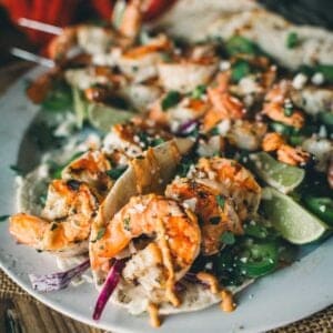 A plate of shrimp tacos garnished with herbs and a side of sliced limes.