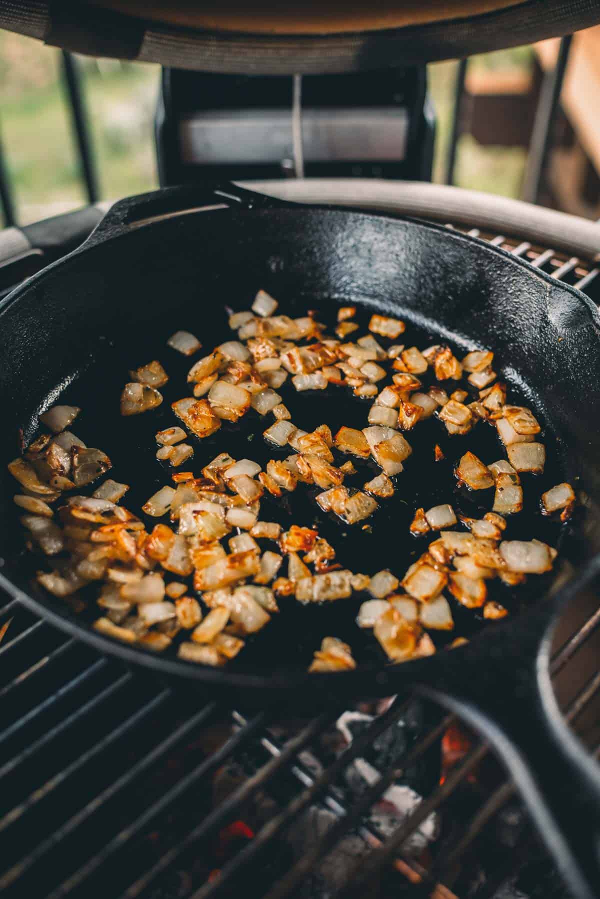 Chopped onions being sautéed in a black cast-iron skillet on the grill.