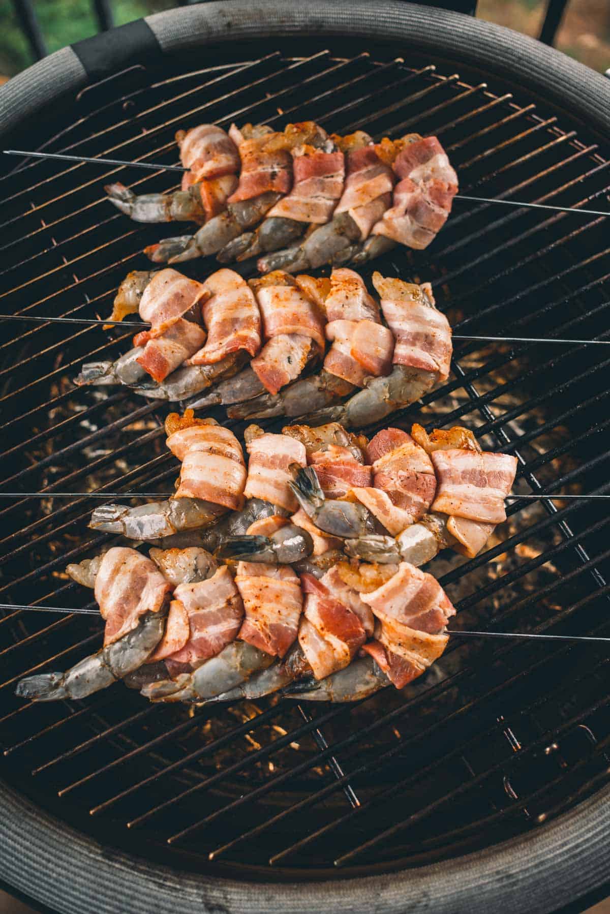 Skewers of shrimp wrapped in bacon are being grilled on a barbecue grill.