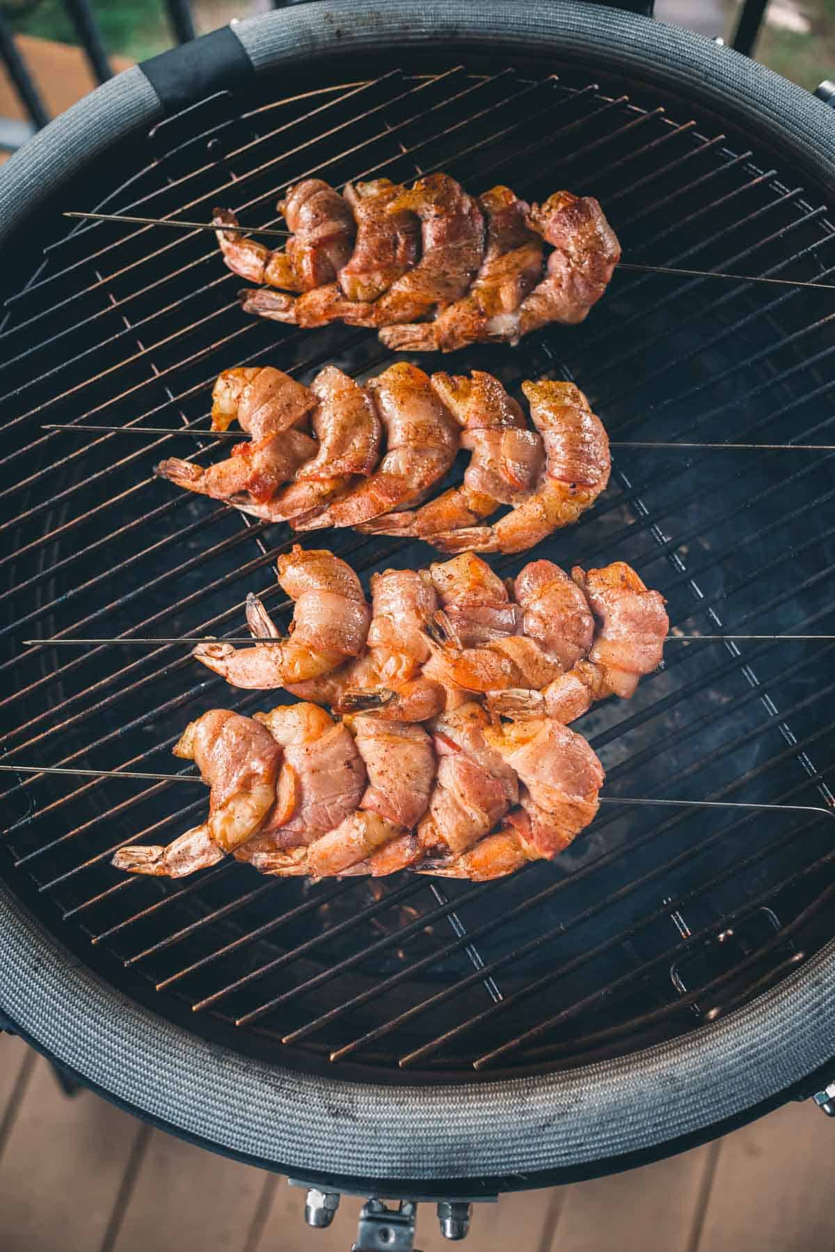 Three skewers of seasoned shrimp are grilling on a round barbecue grill.