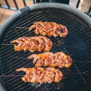 Four skewers of bacon wrapped shrimp are grilling on a barbecue grill.