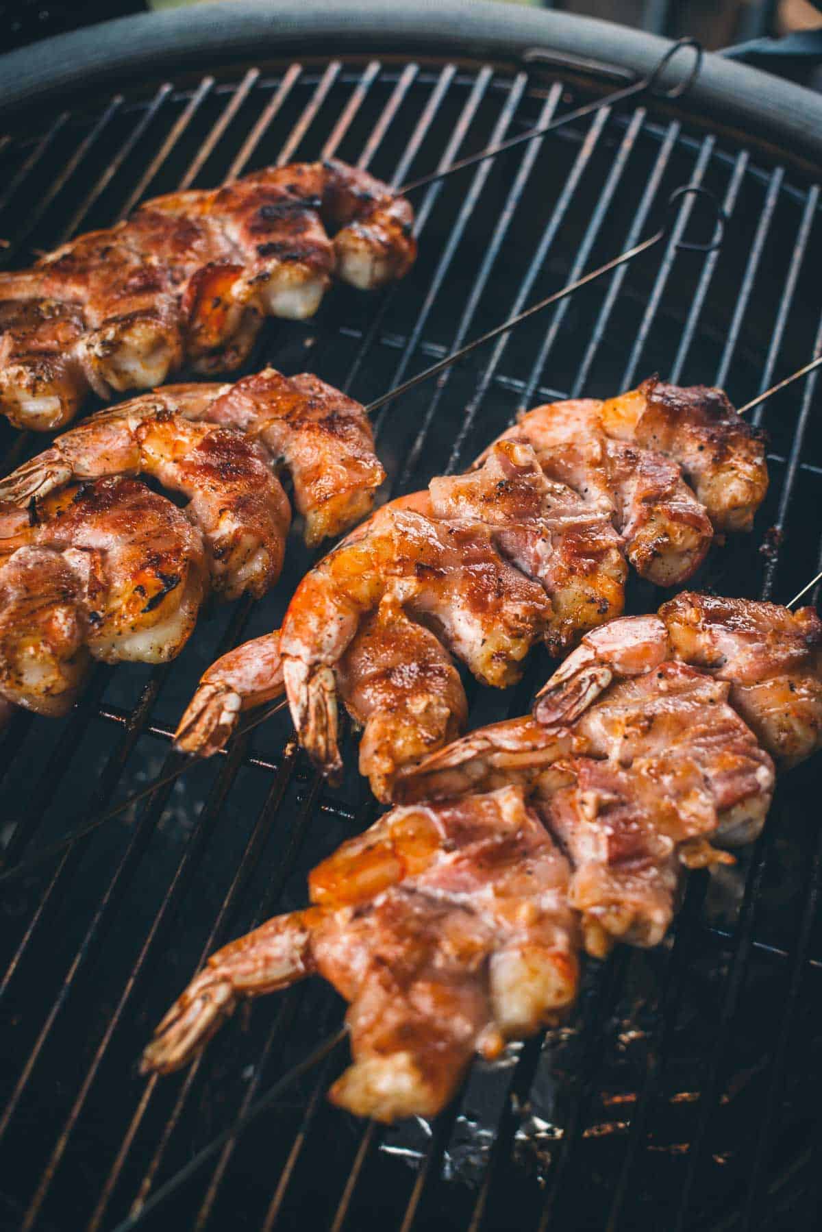 Four skewers of seasoned shrimp are being grilled over a charcoal grill.