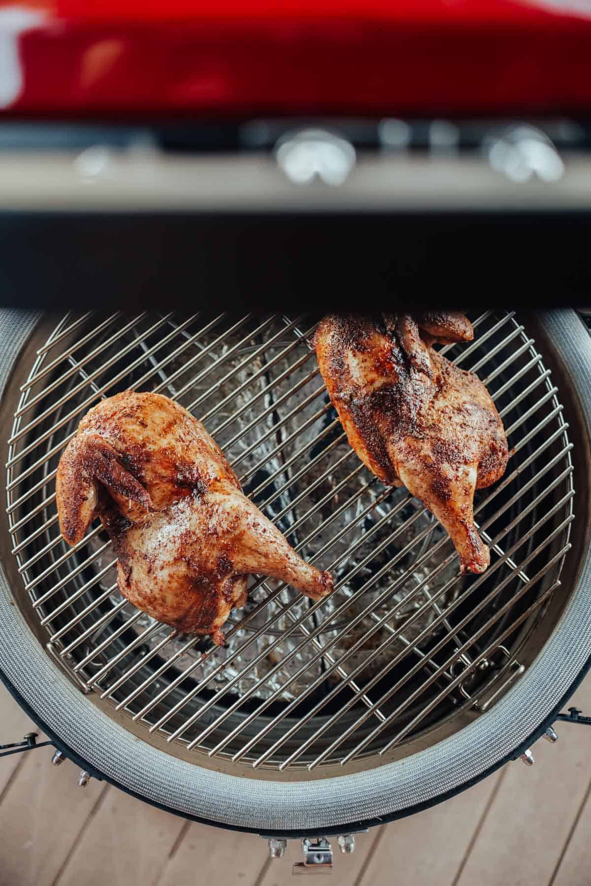 Two seasoned and cooked chicken halves on a round grill grate, viewed from above.