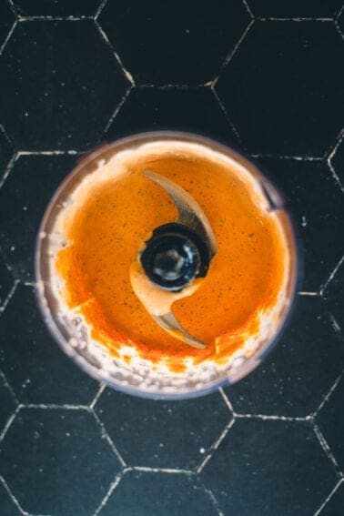 Top-down view of a blender with orange sauce inside, placed on a black tile surface.
