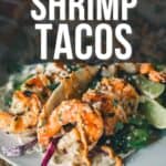 Close-up of three grilled shrimp tacos with vegetables, garnished with sauce and lime slices on a white plate. Text at the top says, "How to Make Grilled Shrimp Tacos image for Pinterest.