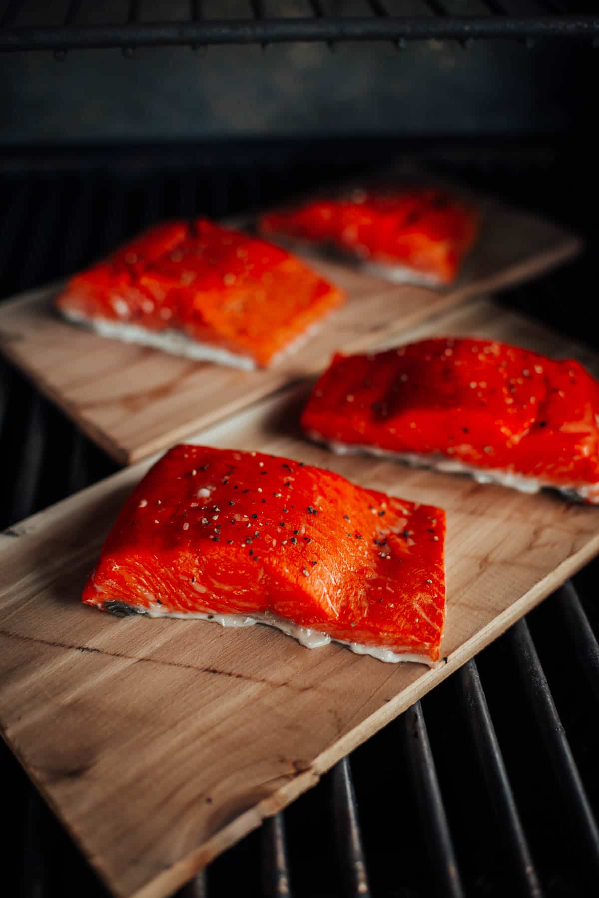 Four pieces of seasoned salmon fillets are placed on wooden planks, ready to be smoked or grilled.