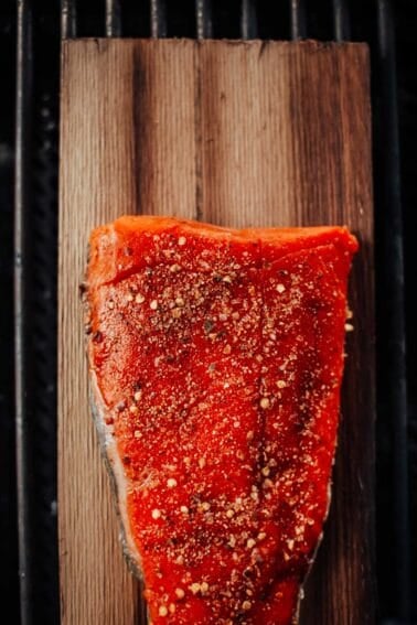 A seasoned, raw salmon fillet on a wooden plank, positioned on a grill.
