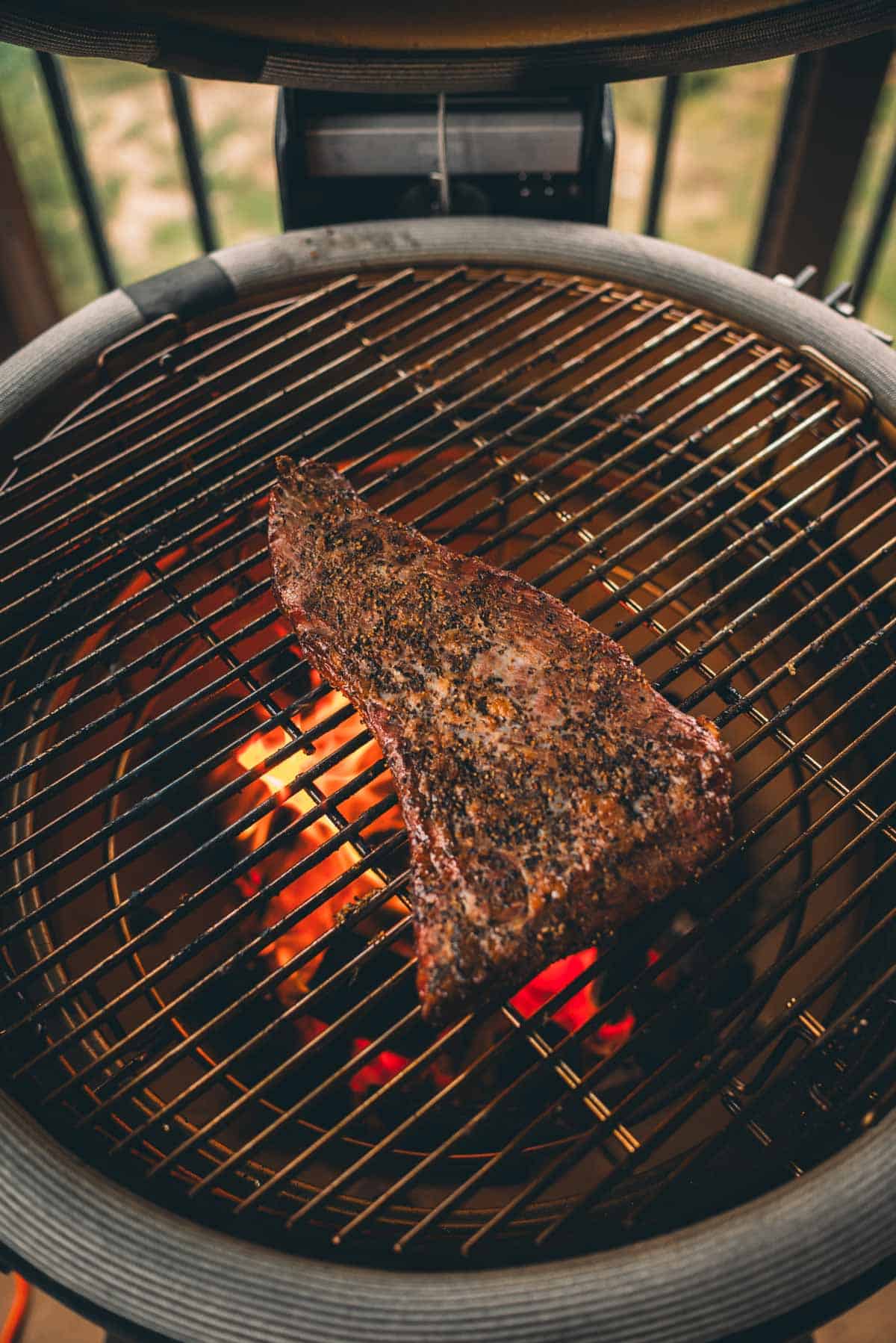 A tri-tip searing on a barbecue with visible flames and coals underneath.