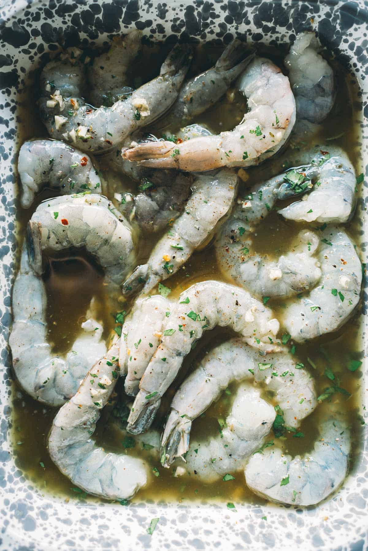 Uncooked shrimp marinating within a speckled ceramic dish.