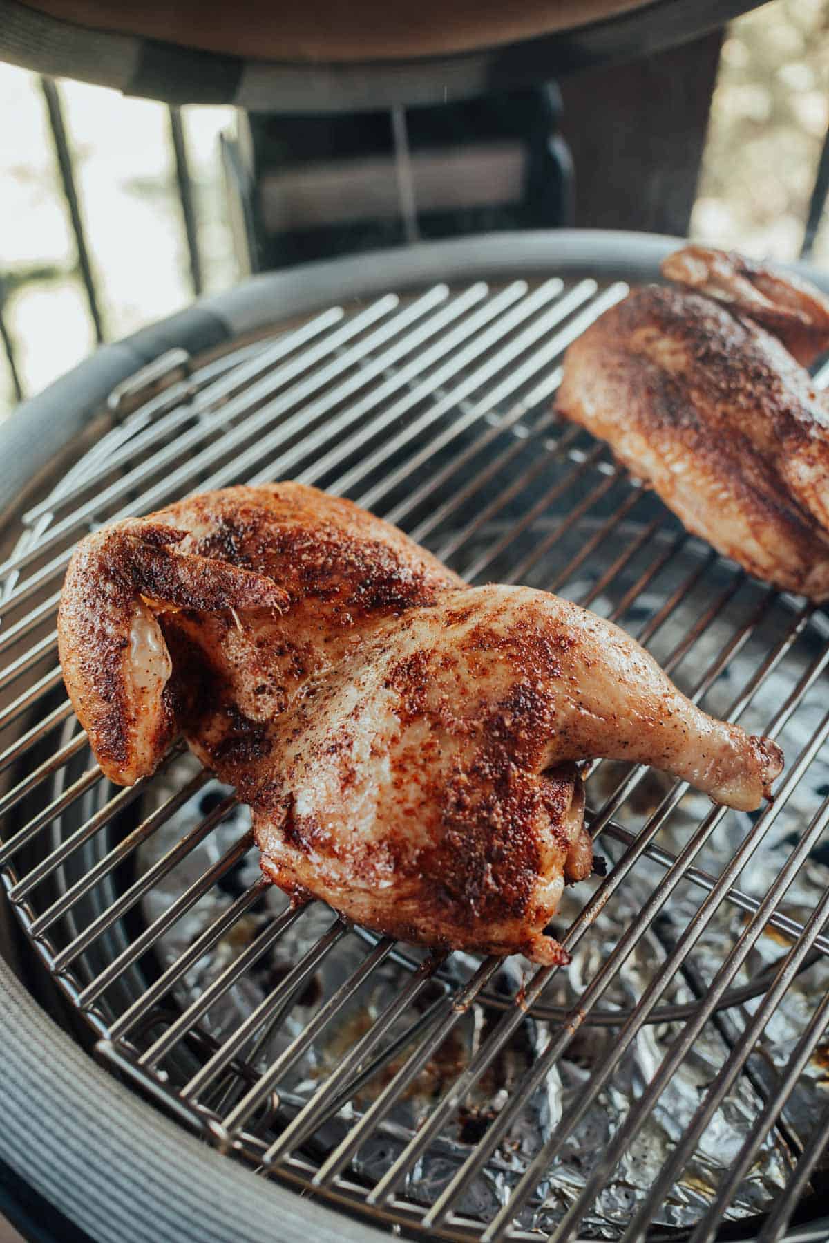 A seasoned grilled chicken half cooking on a round barbecue grill.