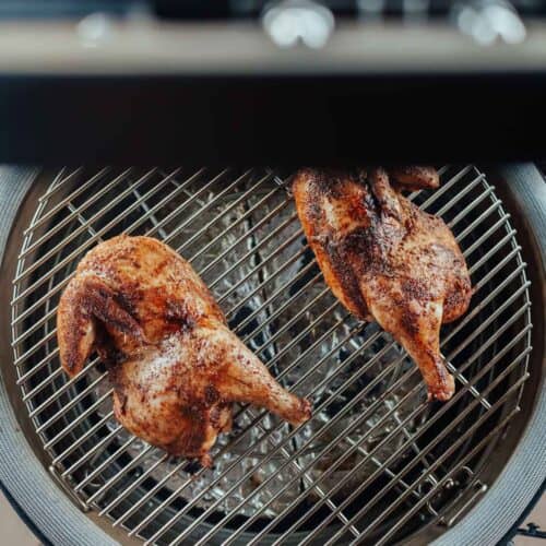 Top view of two whole chickens being grilled on a circular metal grill with a red exterior.