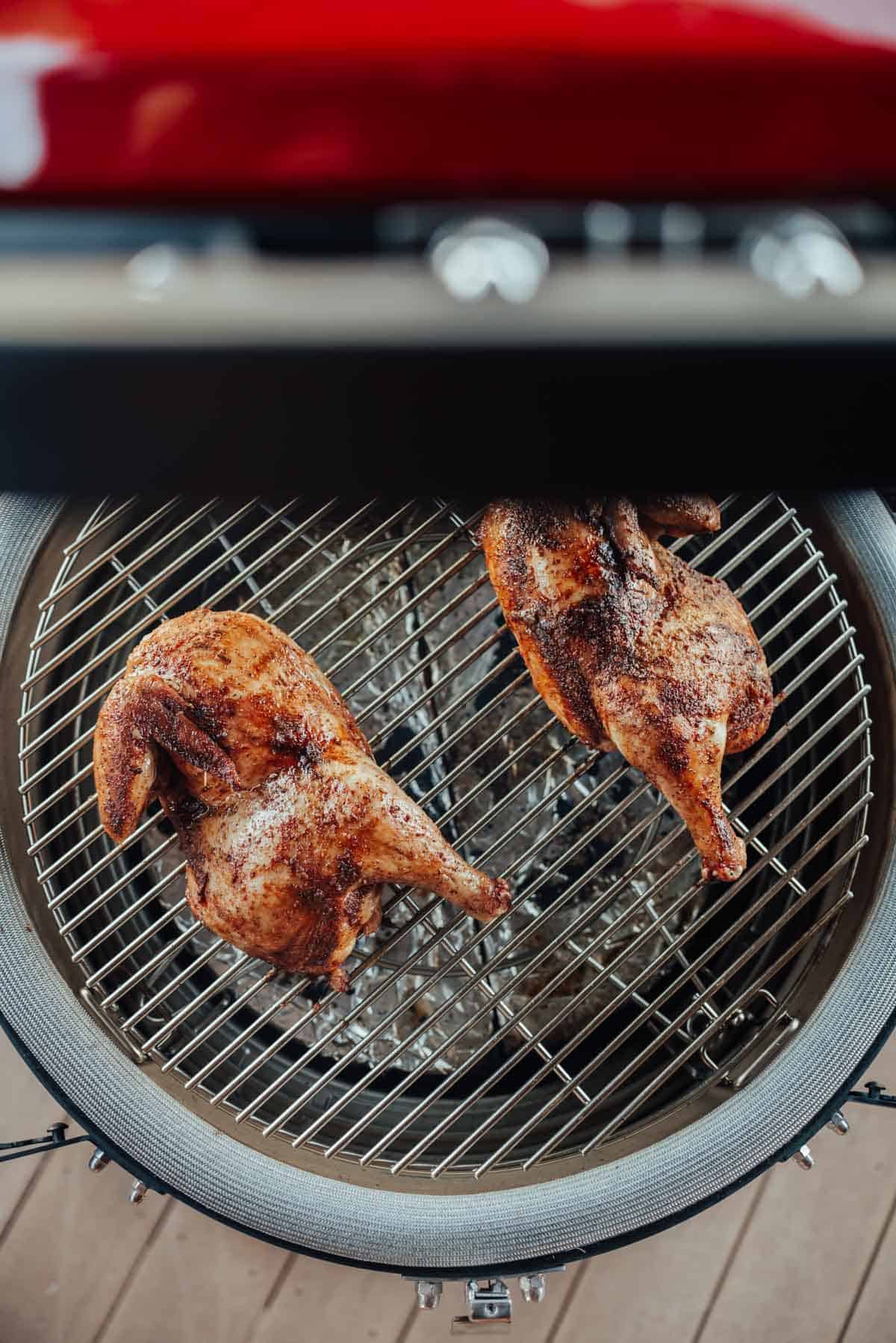 Top view of two whole chickens being grilled on a circular metal grill with a red exterior.