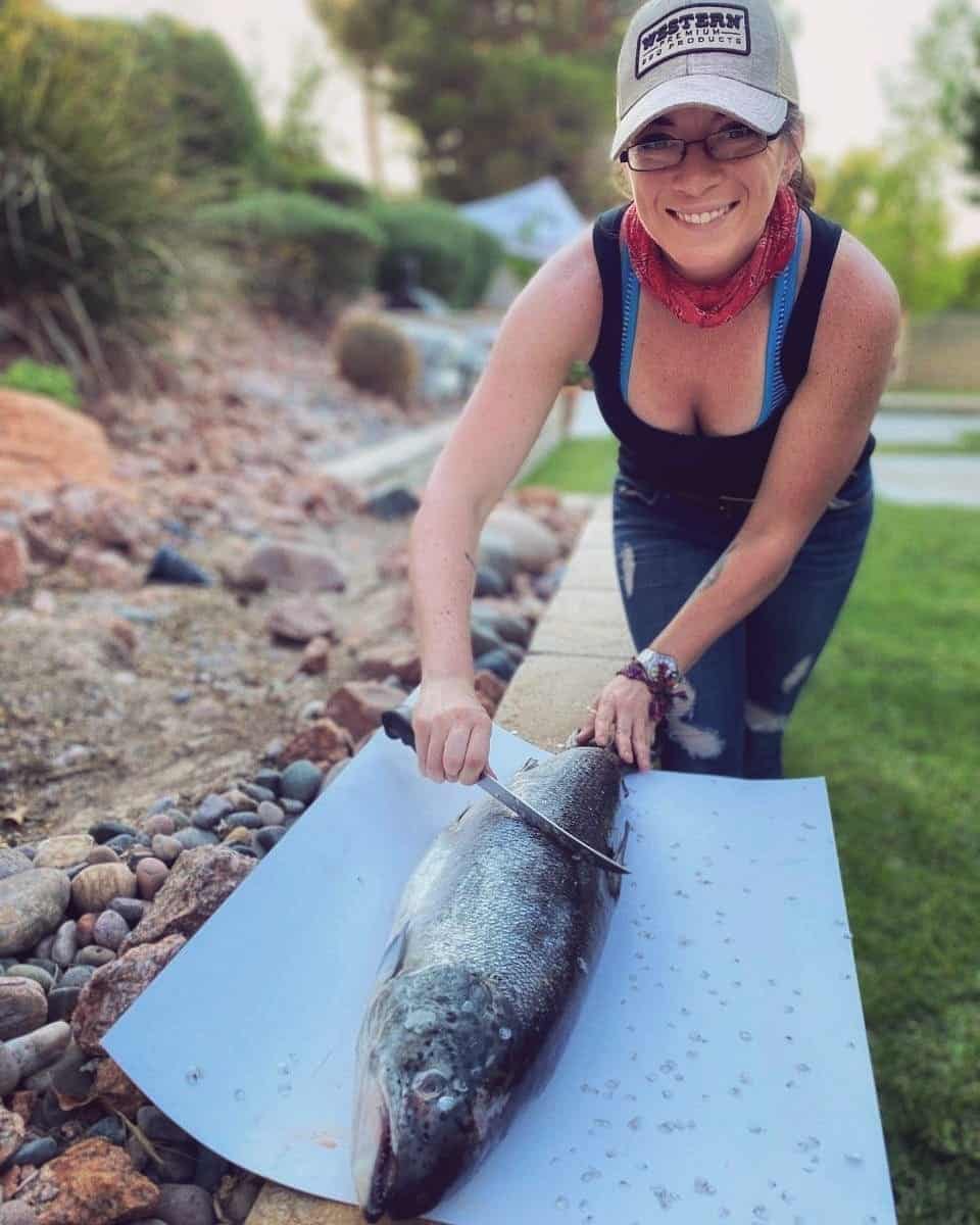 A person in a hat and glasses is preparing to cut a large fish on a white surface outdoors.