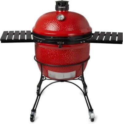 A red Kamado Joe charcoal grill featuring a temperature gauge, dual side metal shelves, and a wheeled metal stand. Perfect for anyone learning how to use a kamado grill.