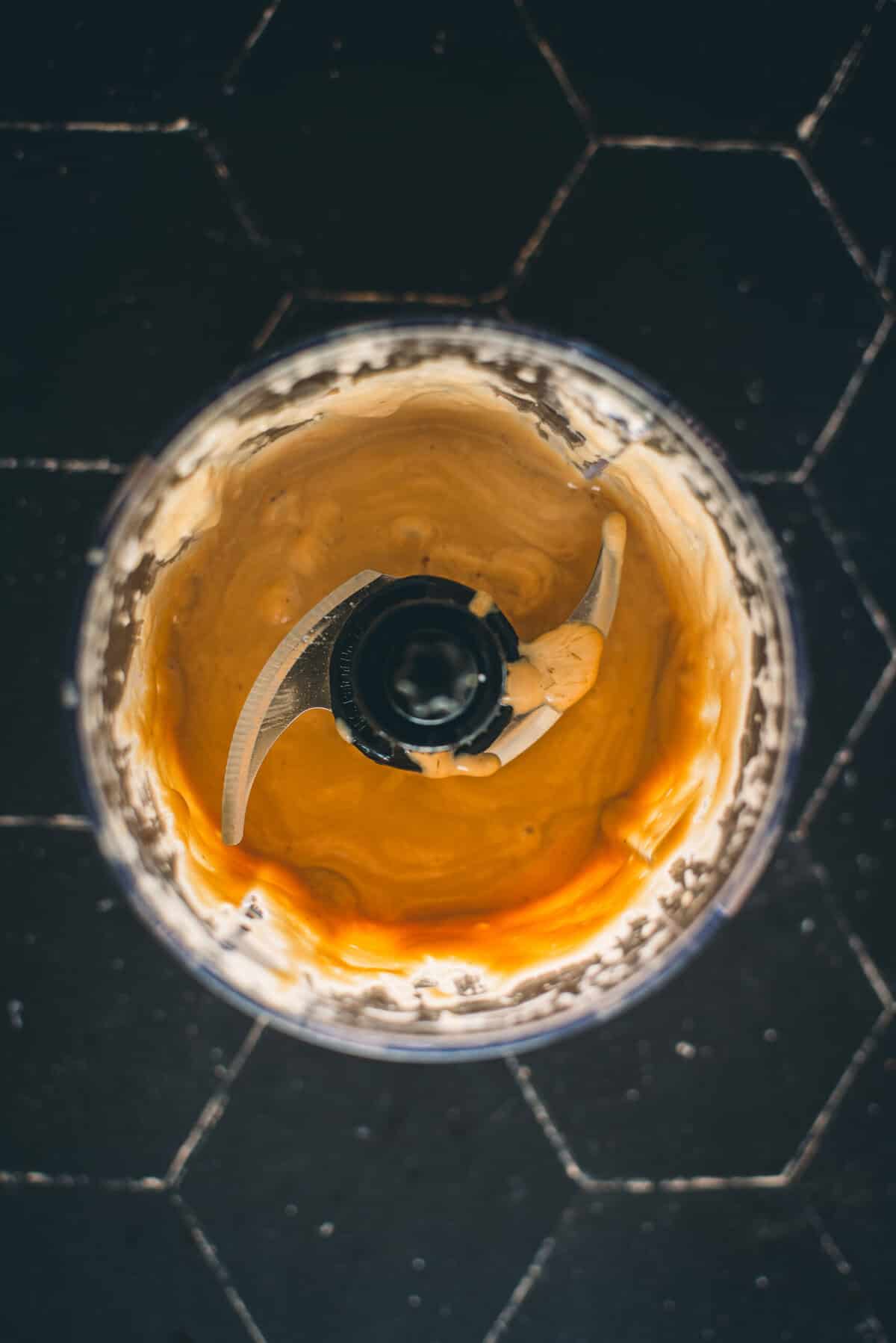 Top view of a blender with a creamy Caesar dressing mixture inside.