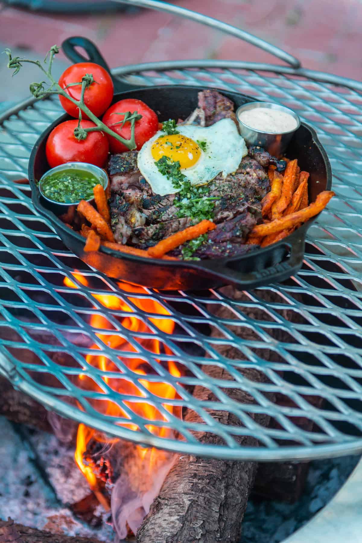 A cast iron skillet is cooking over an open flame grill in the camp kitchen. 