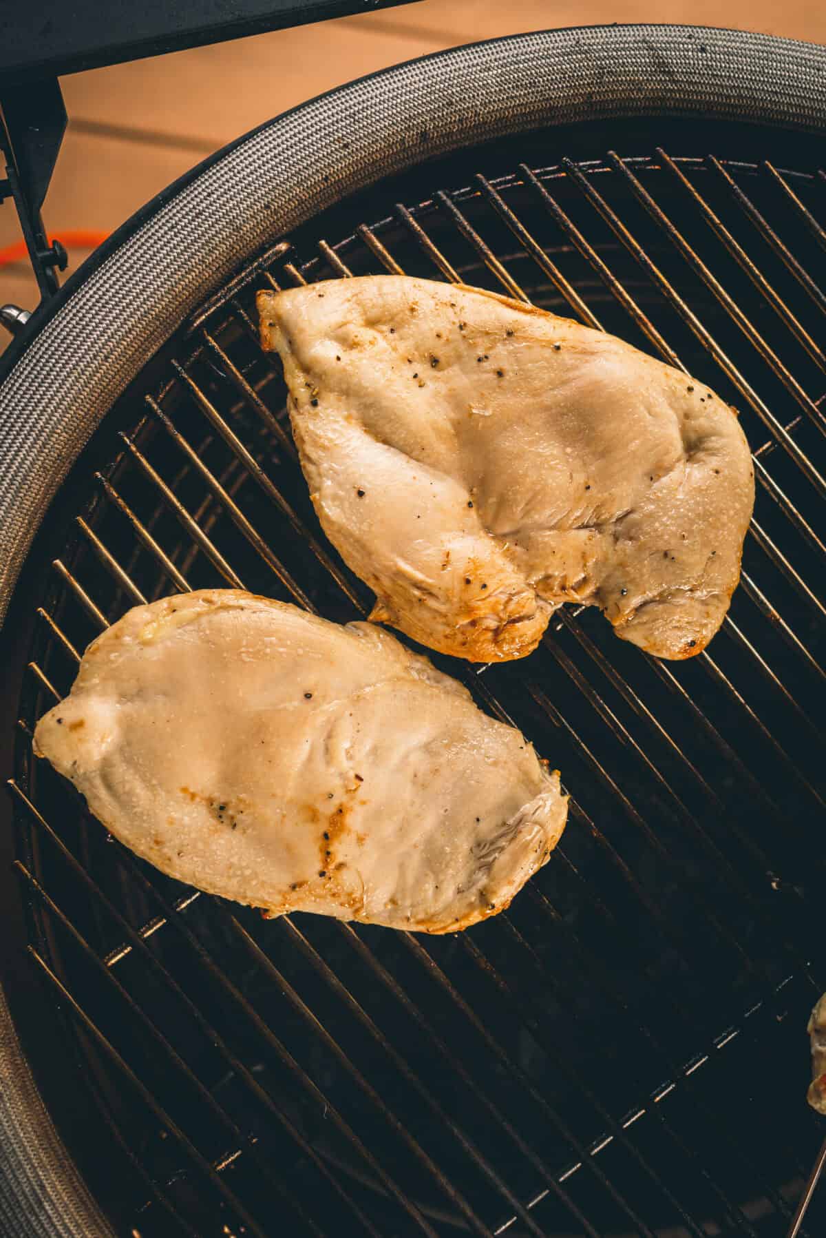 Two seasoned chicken breasts on a grill, cooking over charcoal.