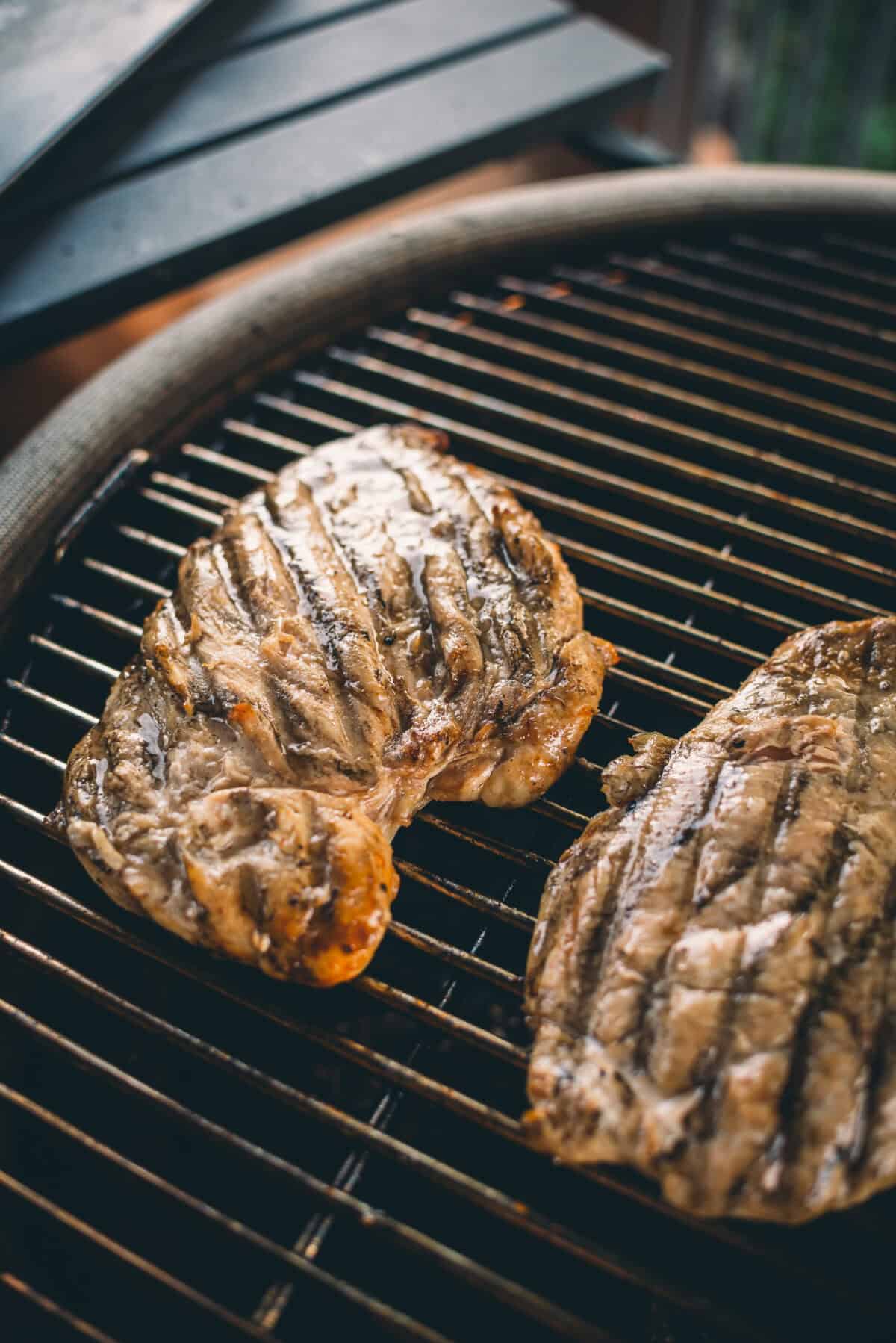 Two chicken breasts cooking on a grill with visible sear marks.