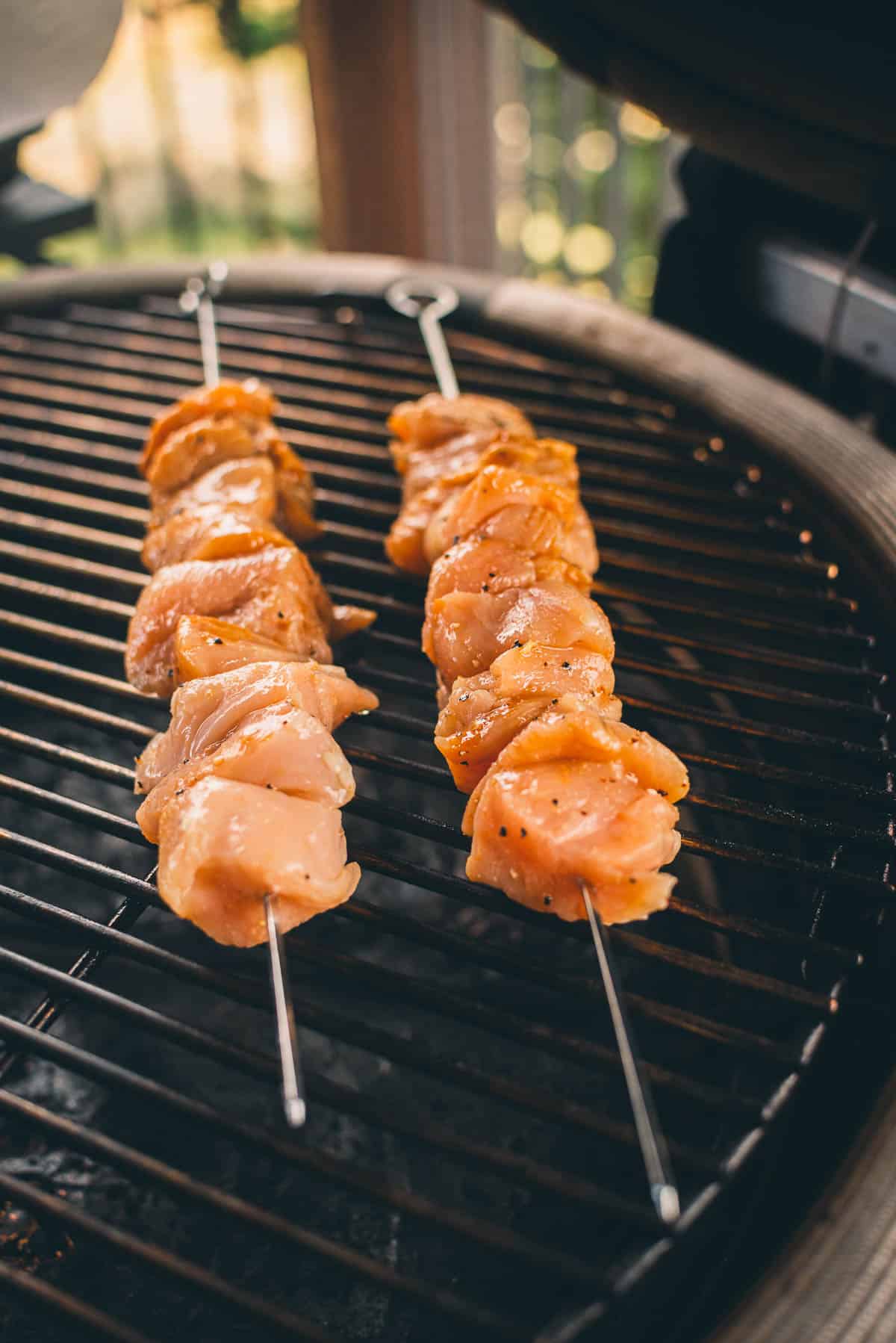 Two skewers of marinated chicken pieces are being grilled over an outdoor barbecue.